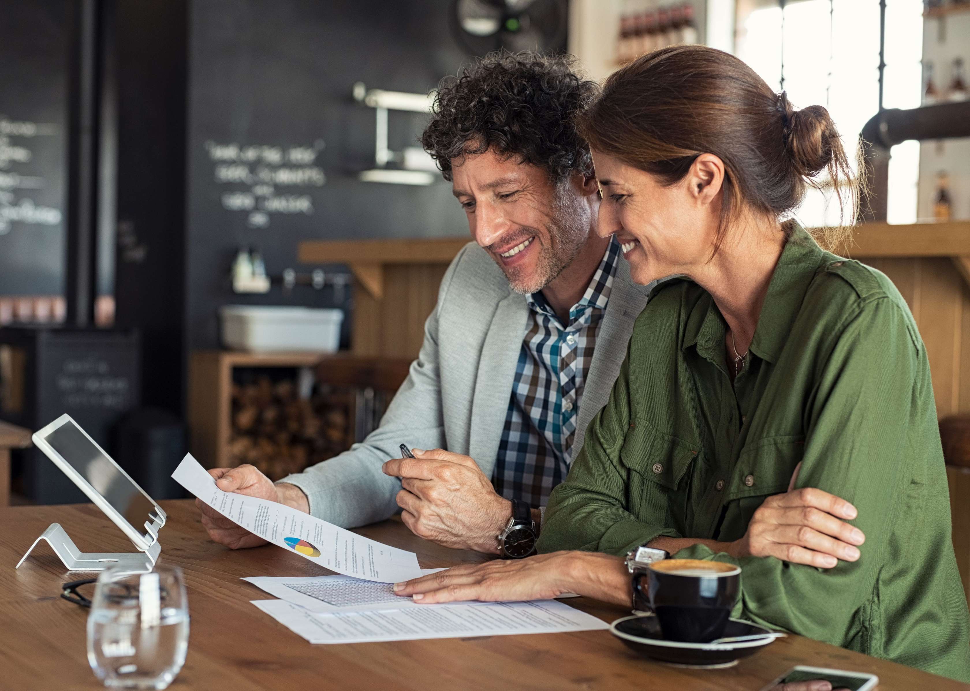 Frau und Mann sitzen lächelnd mit Dokumenten im Café