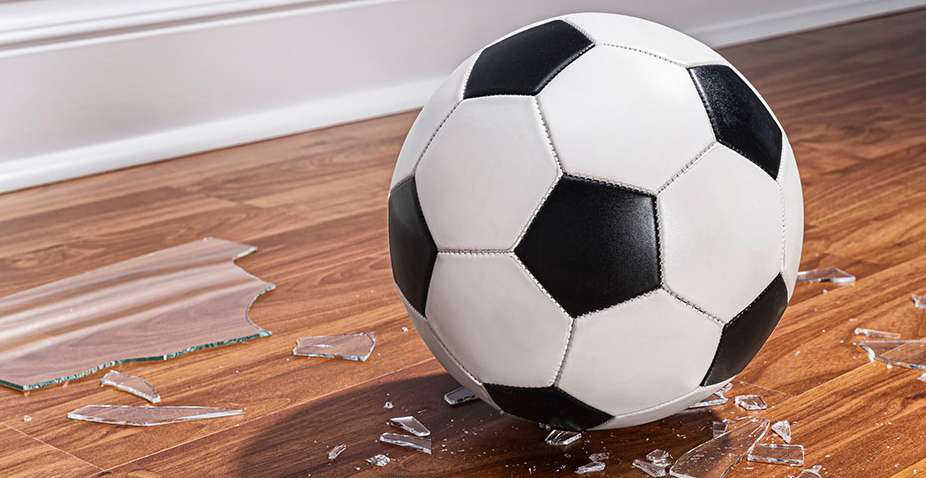 Fußball liegt zwischen Glasscherben auf einem Holzfußboden. Foto: iStock/cmannphoto