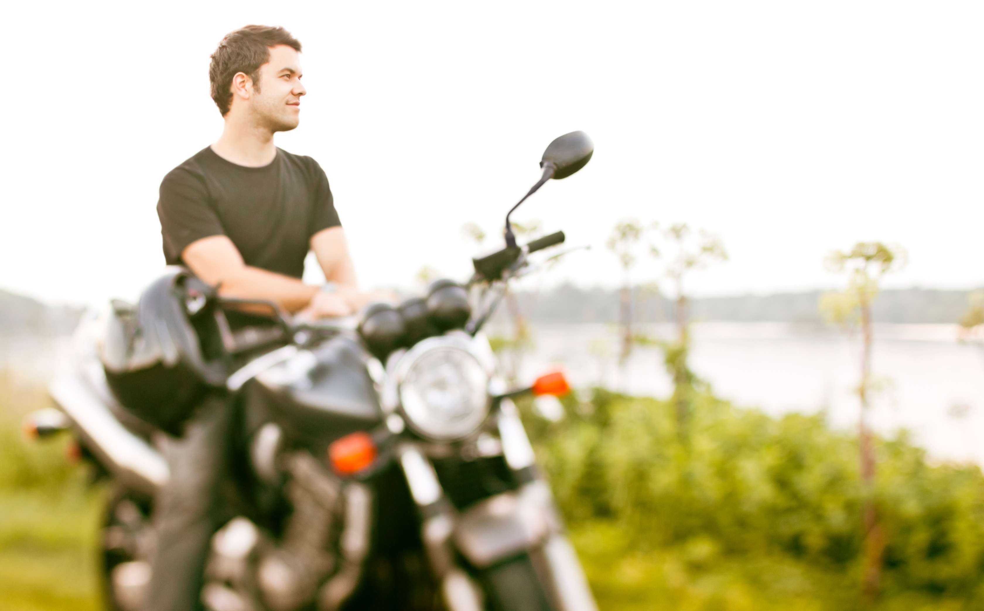 Motorrad Versicherung: Mann sitzt auf Motorrad und blickt auf See.