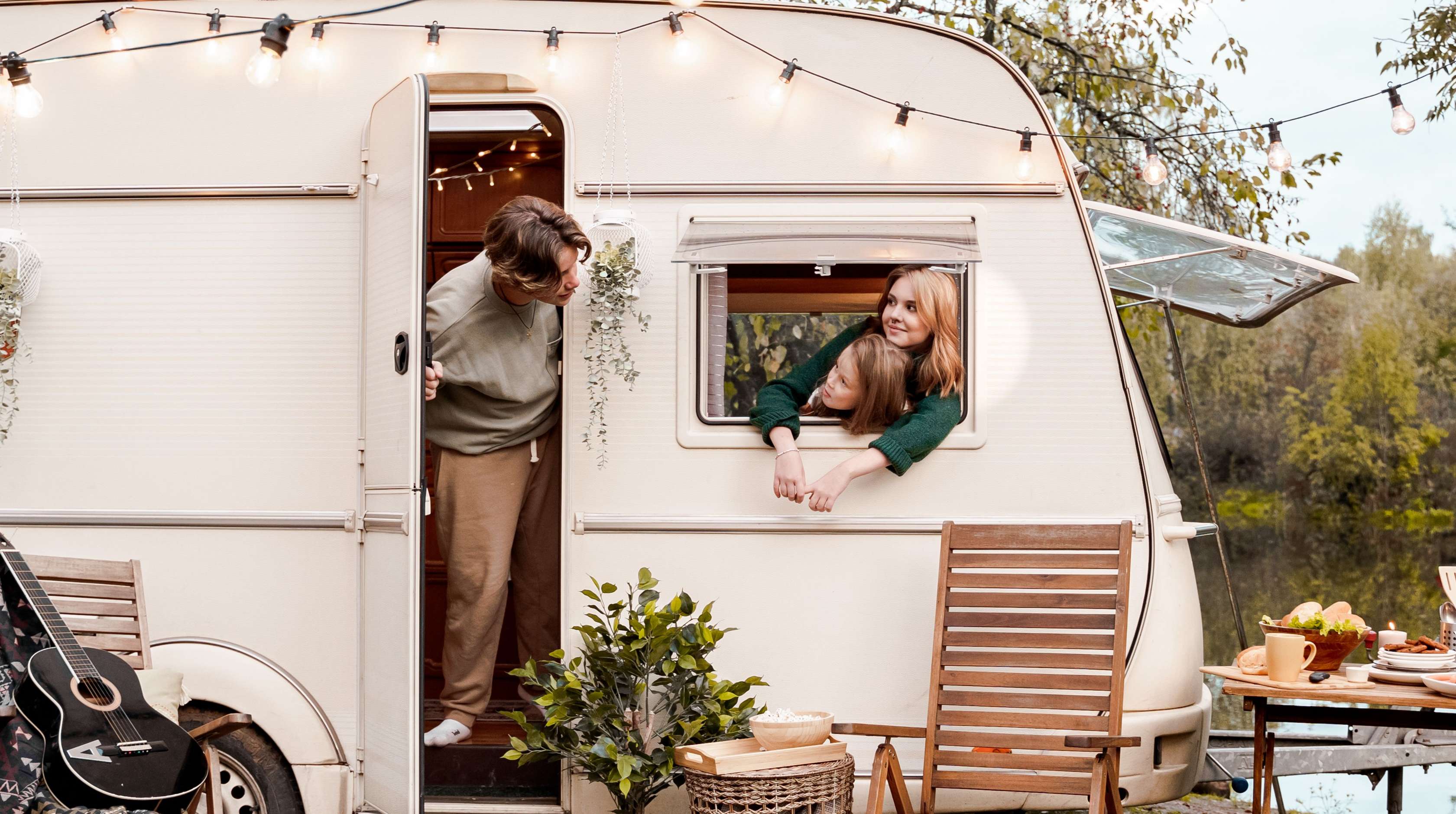 Allianz - Wohnwagenversicherung Angebot: Ein junger Mann schaut aus der Tür eines Wohnwagens, während eine junge Frau fröhlich aus dem Fenster lehnt.