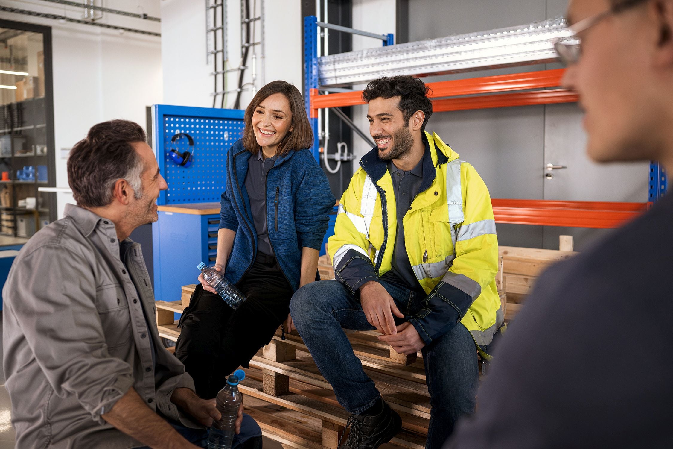 Allianz - Betriebliche Krankenversicherung Angebot:  Ein älterer Mann mit grauem Bart und eine Frau mit Locken und Gehörschutz um den hals geben sich in einer Werkstatt für Holzverarbeitung lächelnd die Hand.