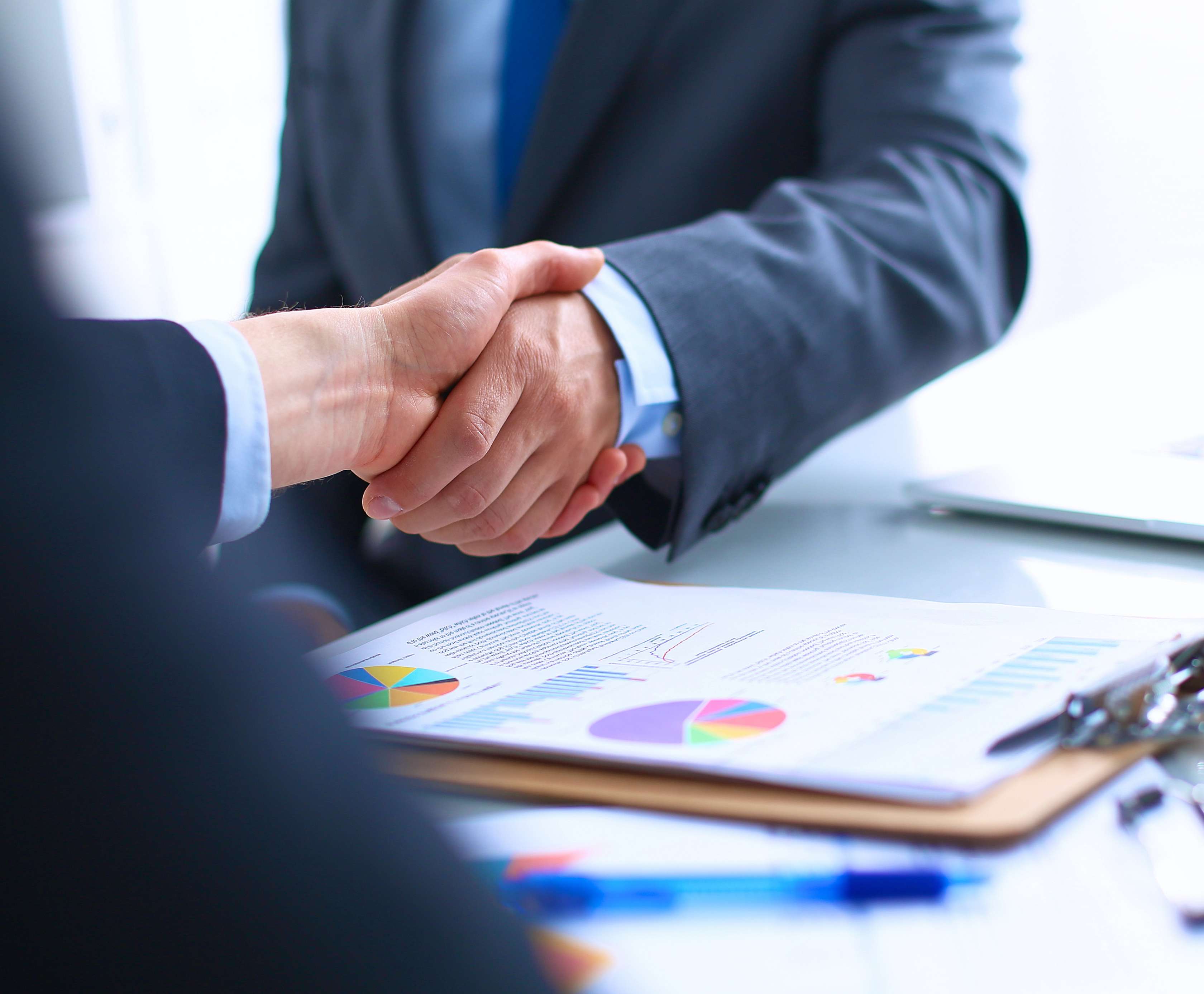 Allianz Vertrauensschadenversicherung | Zwei Geschäftsmänner schütteln sich die Hände. Auf dem Schreibtisch liegen zahlreiche Unterlagen mit Diagrammen.