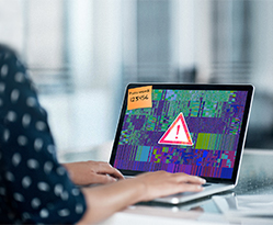 Allianz - Cyberversicherung für Unternehmen: Eine Frau sitzt an einem Schreibtisch an einem Laptop, auf dem ein Warndreieck abgebildet ist.