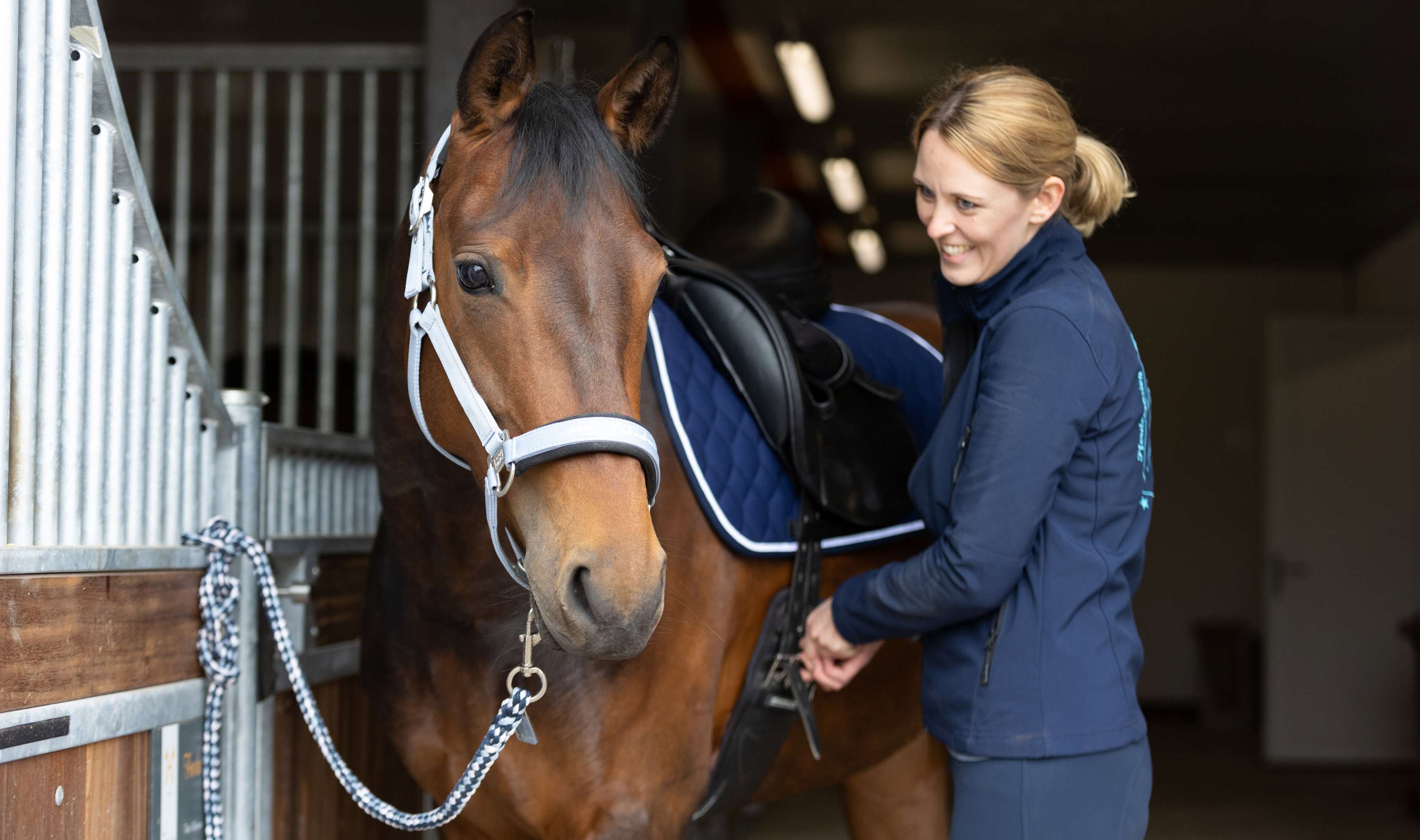 Pferdekrankenversicherung Vollschutz: Eine Frau sattelt ein Pferd in einem Stall.