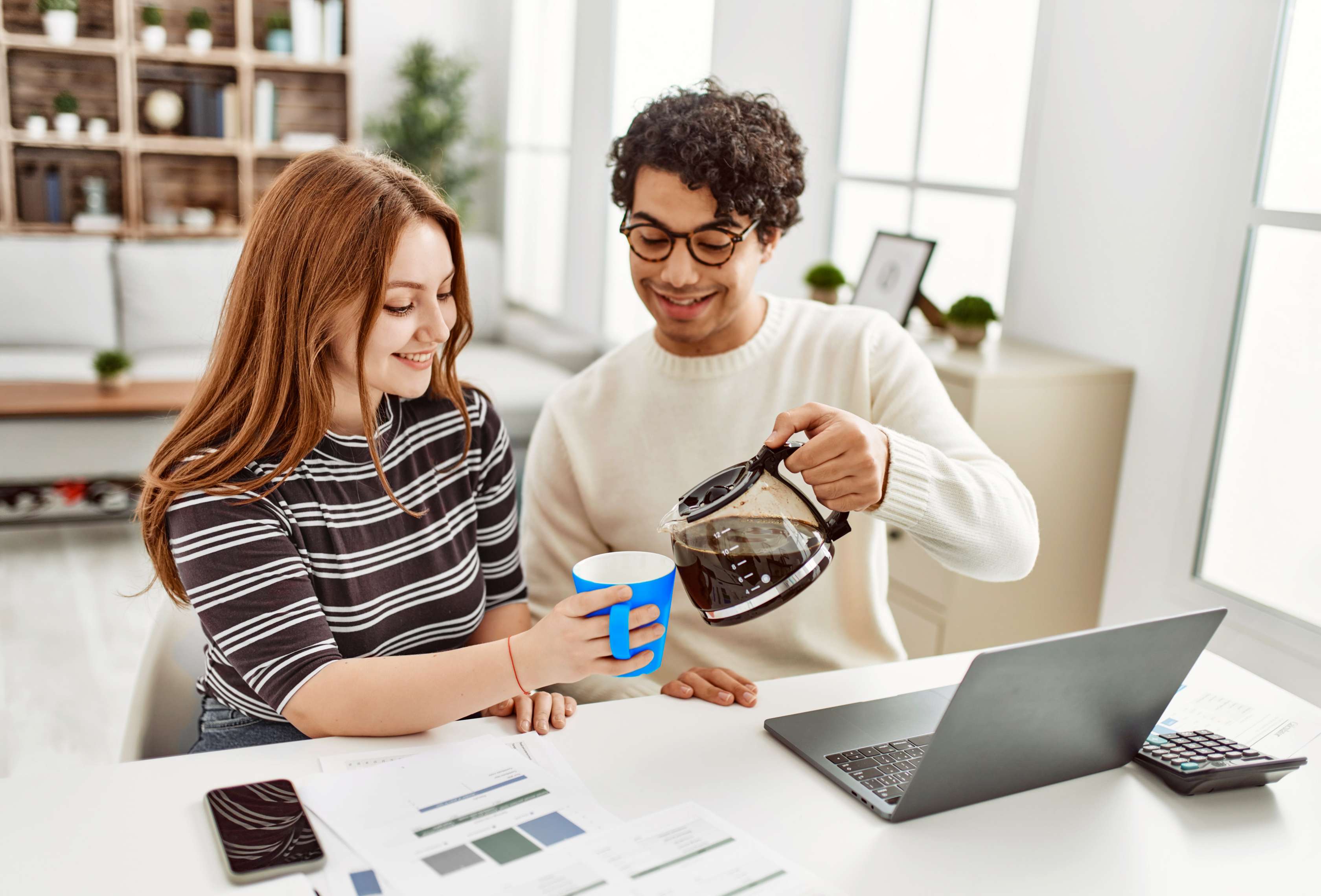 Allianz Privathaftpflicht: Ein junger Mann sitzt neben einer jungen Frau an einem Laptop, während er ihr Kaffee in eine Tasse schenkt