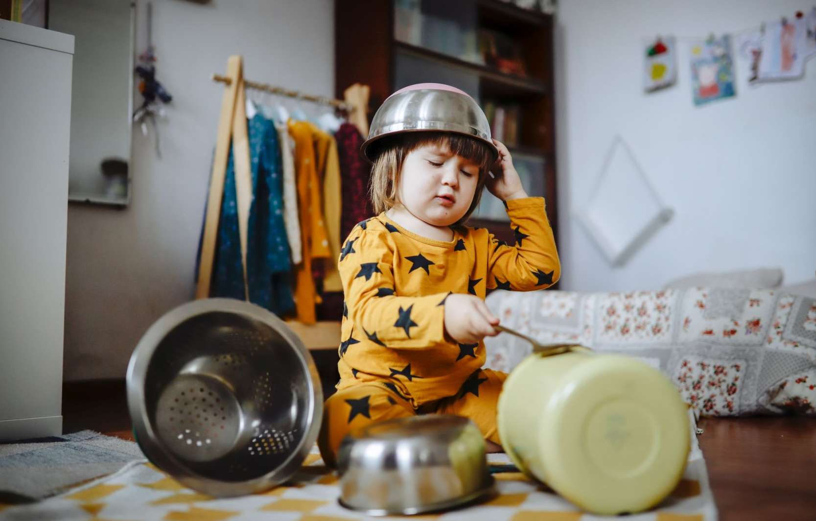 Allianz Kleine Helden: Ein Kleinkind mit einem Topf auf dem Kopf schlägt mit einem Löffel auf einen weiteren Topf