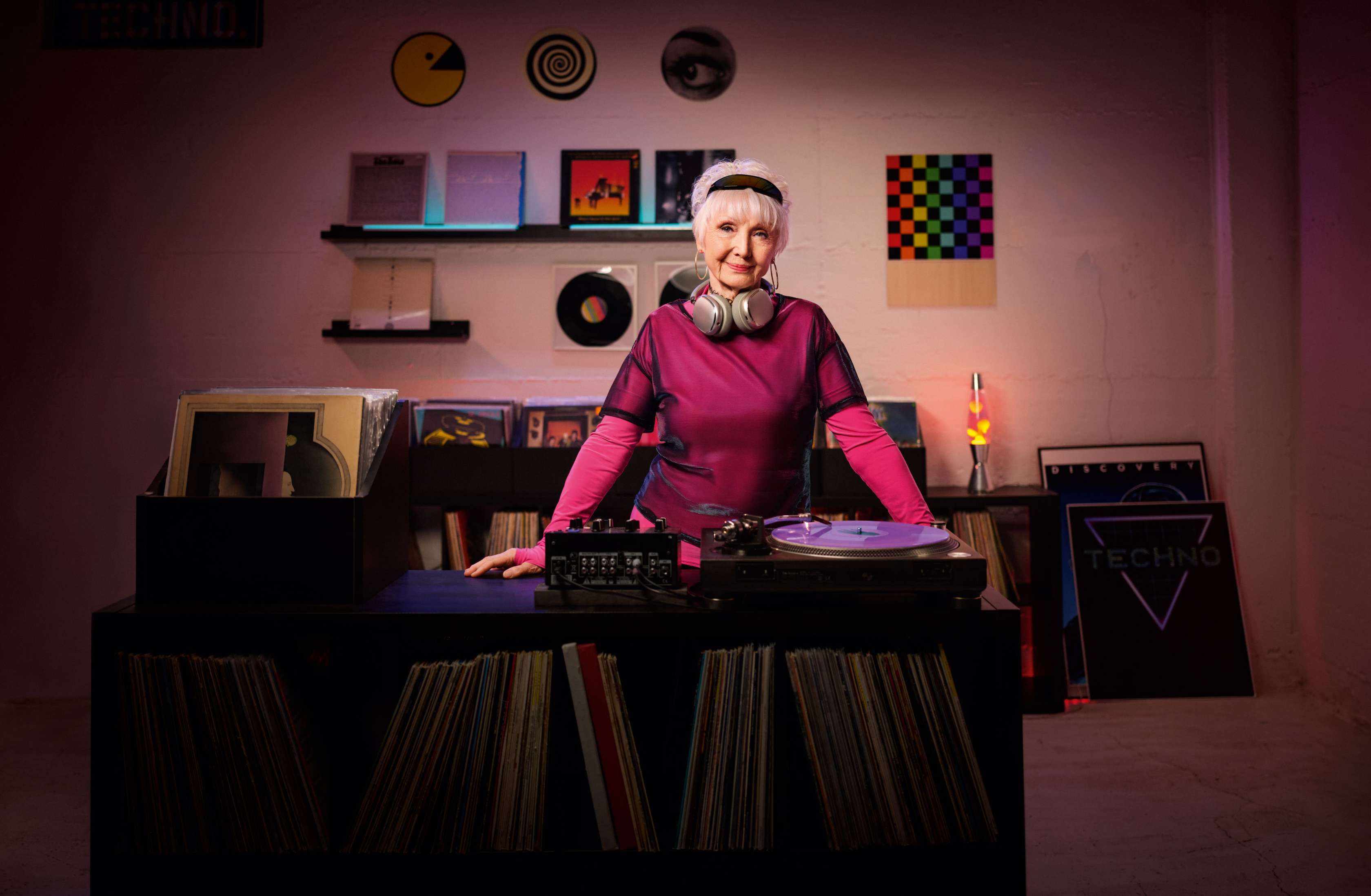 Allianz Pflegezusatzversicherung Kooperationsangebot: Eine ältere Dame in pinker Kleidung steht hinter einem DJ-Pult