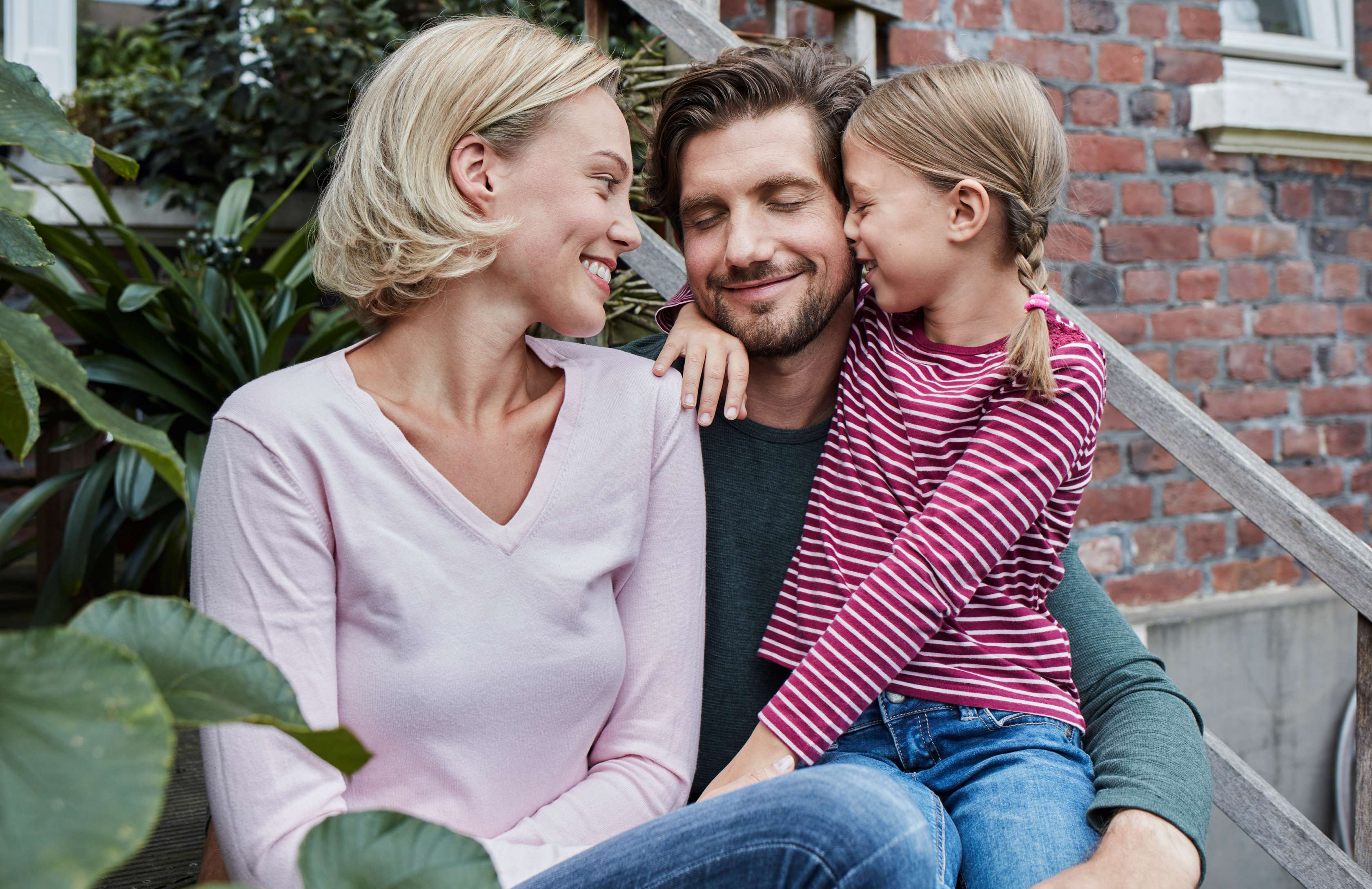Allianz Risiko­lebens­versicherung Kooperationsangebot: Familie kuschelt for einem Haus.