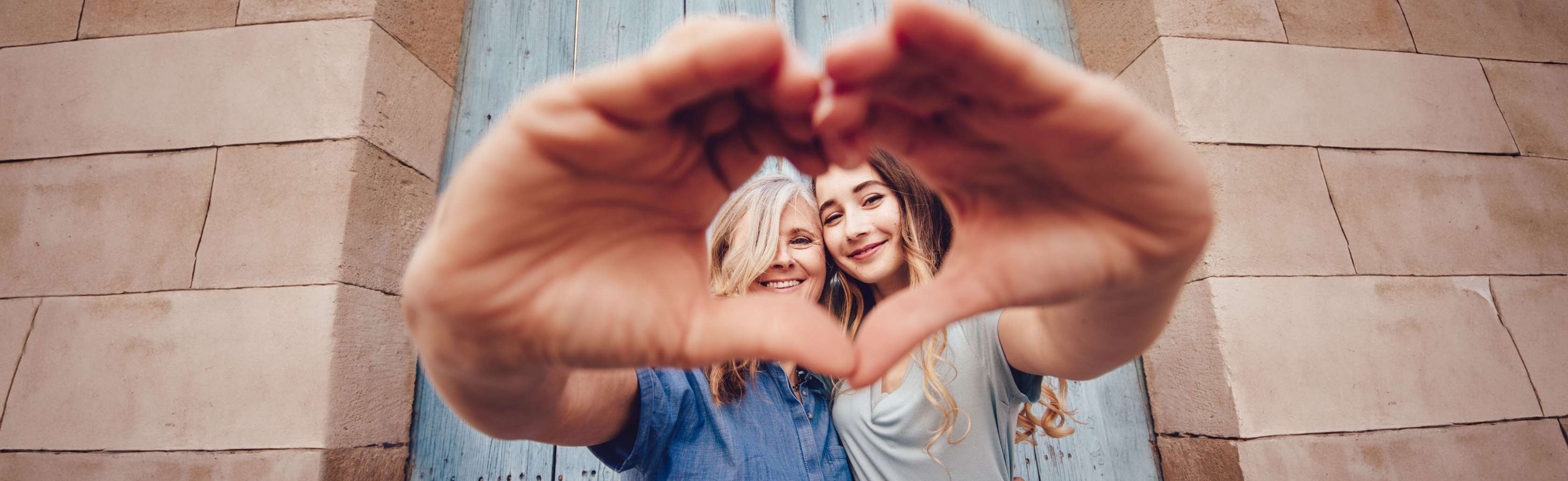 Sterbegeldversicherung: Eine Mutter hält gemeinsam mit ihrer Tochter mit den Händen ein Herz in die Kamera. 