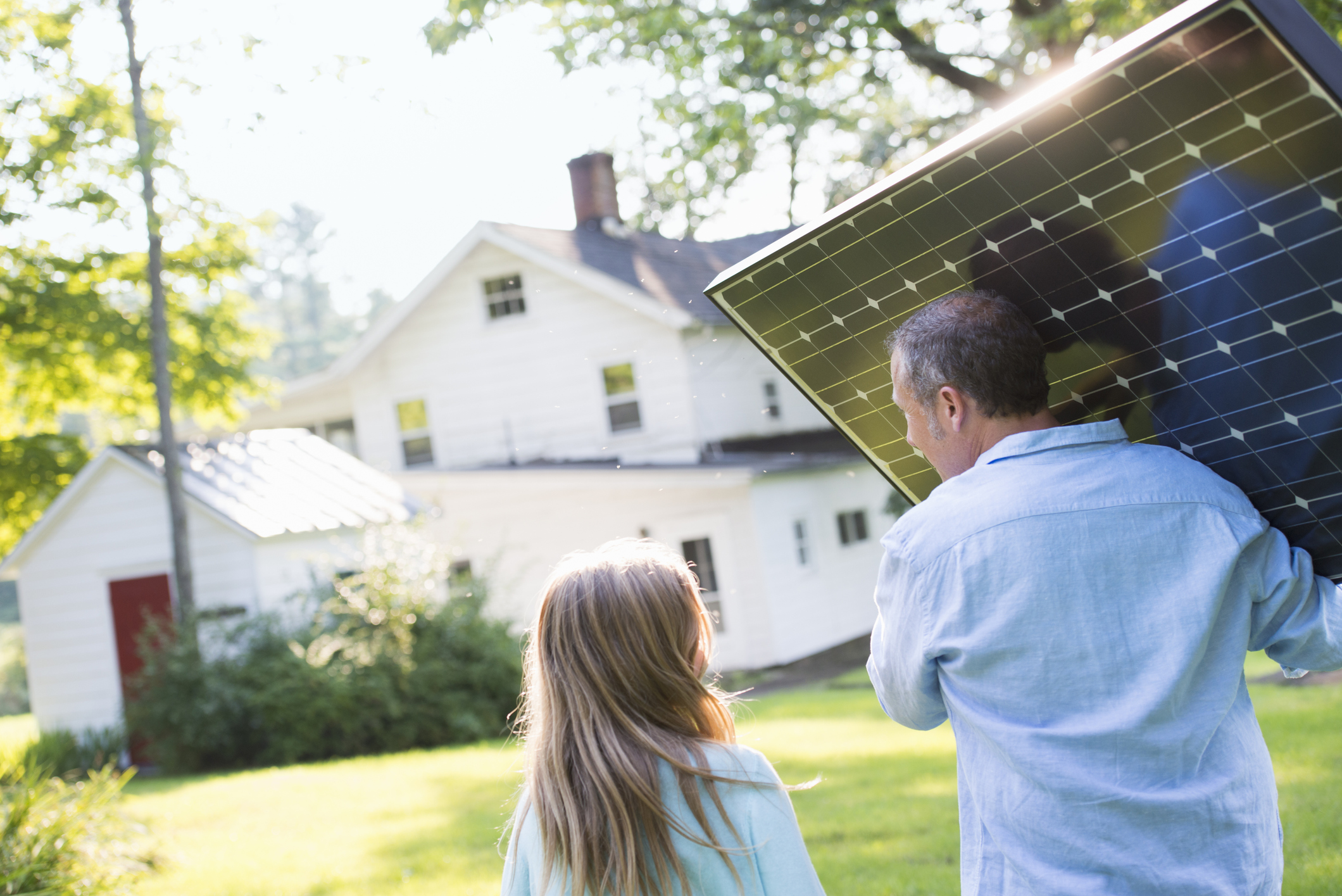 Allianz - Baufinanzierung: Mann trägt Solar-Panel und geht mit Mädchen zu einem weißen Haus