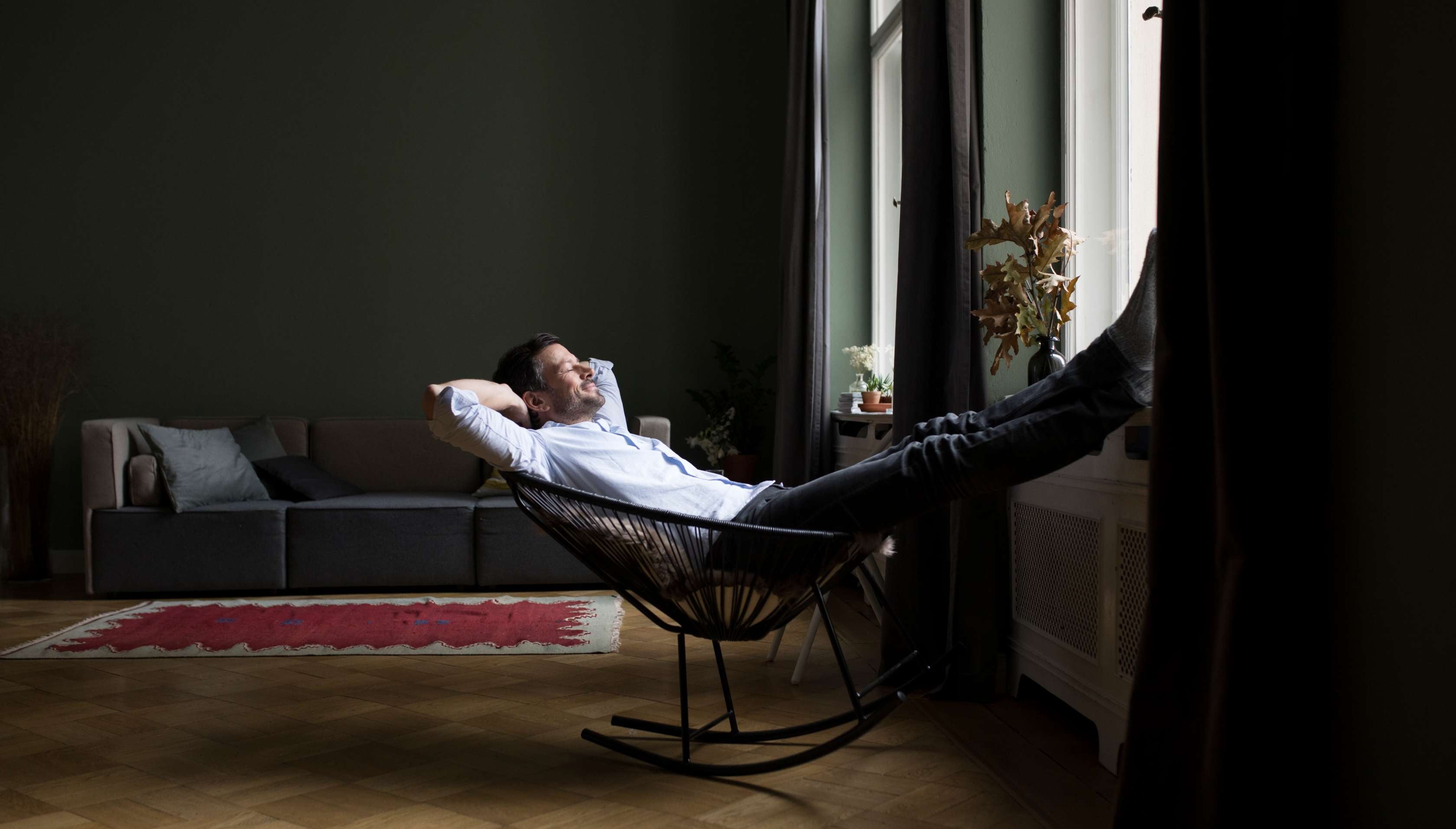 Allianz Hausrat-Haftpflicht-Rechtschutz-Kombi: Mann liegt entspannt lächelnd in einem Sessel im Wohnzimmer.