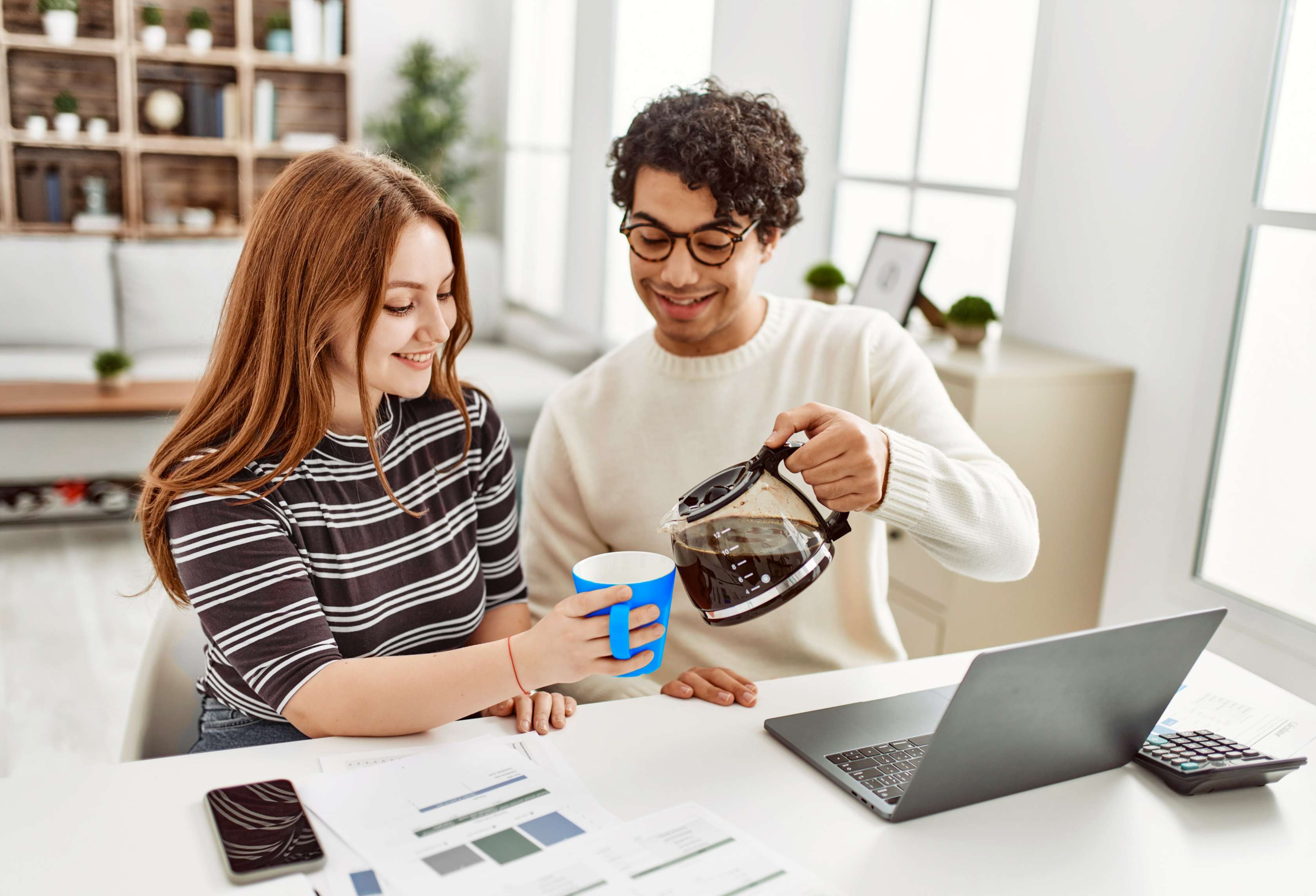Allianz Privathaftpflicht: Ein junger Mann sitzt neben einer jungen Frau an einem Laptop, während er ihr Kaffee in eine Tasse schenkt