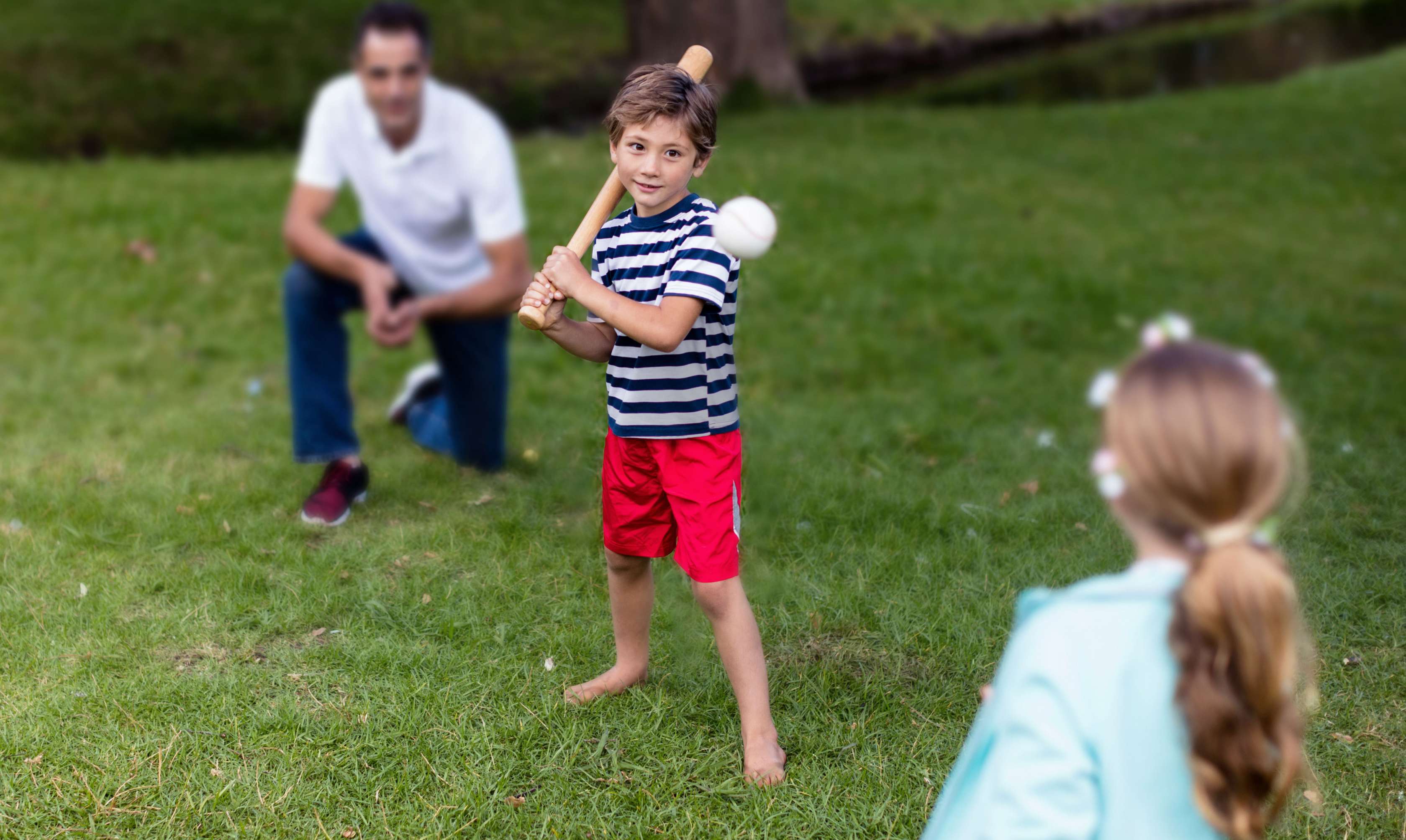 Familienversicherung: Kleiner Junge schlägt nach einem fliegenden Baseball, während der Vater als Fänger hinter ihm kniet
