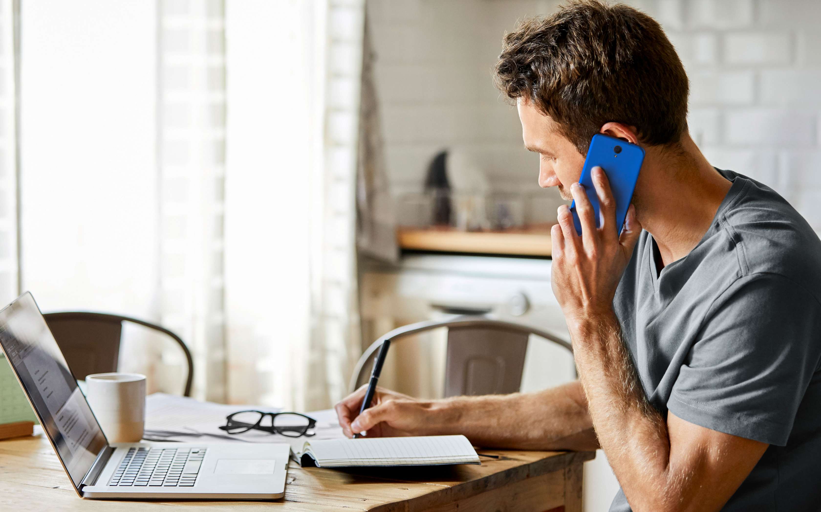 Allianz Privatrechtsschutzversicherung: Mann sitzt telefonierend vor seinem Laptop am Küchentisch.