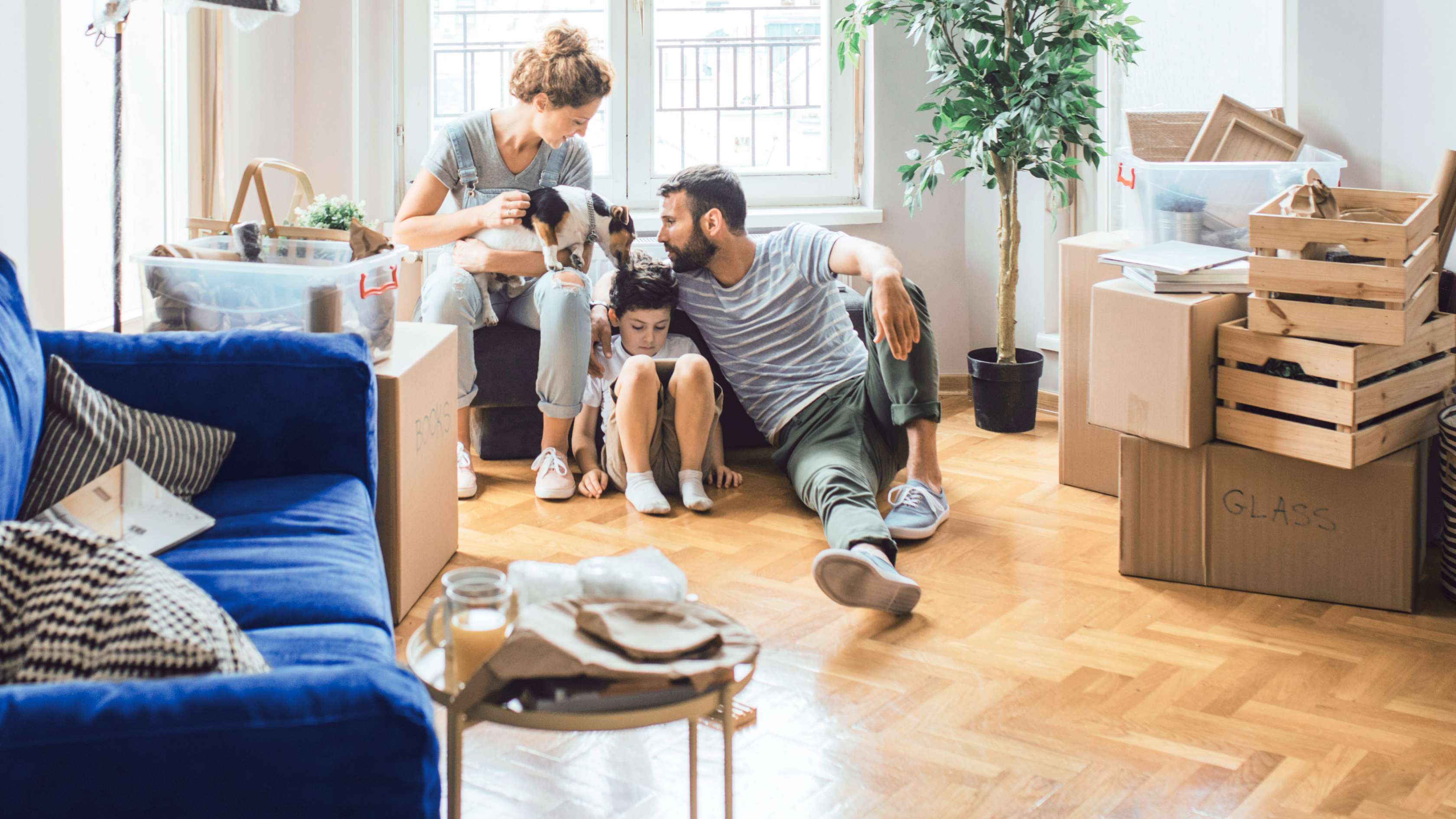 Allianz - Privatschutz Versicherungen kombinieren: Eine Familie sitzt im Wohnzimmer, das mit Umzugskartons gefüllt ist. 