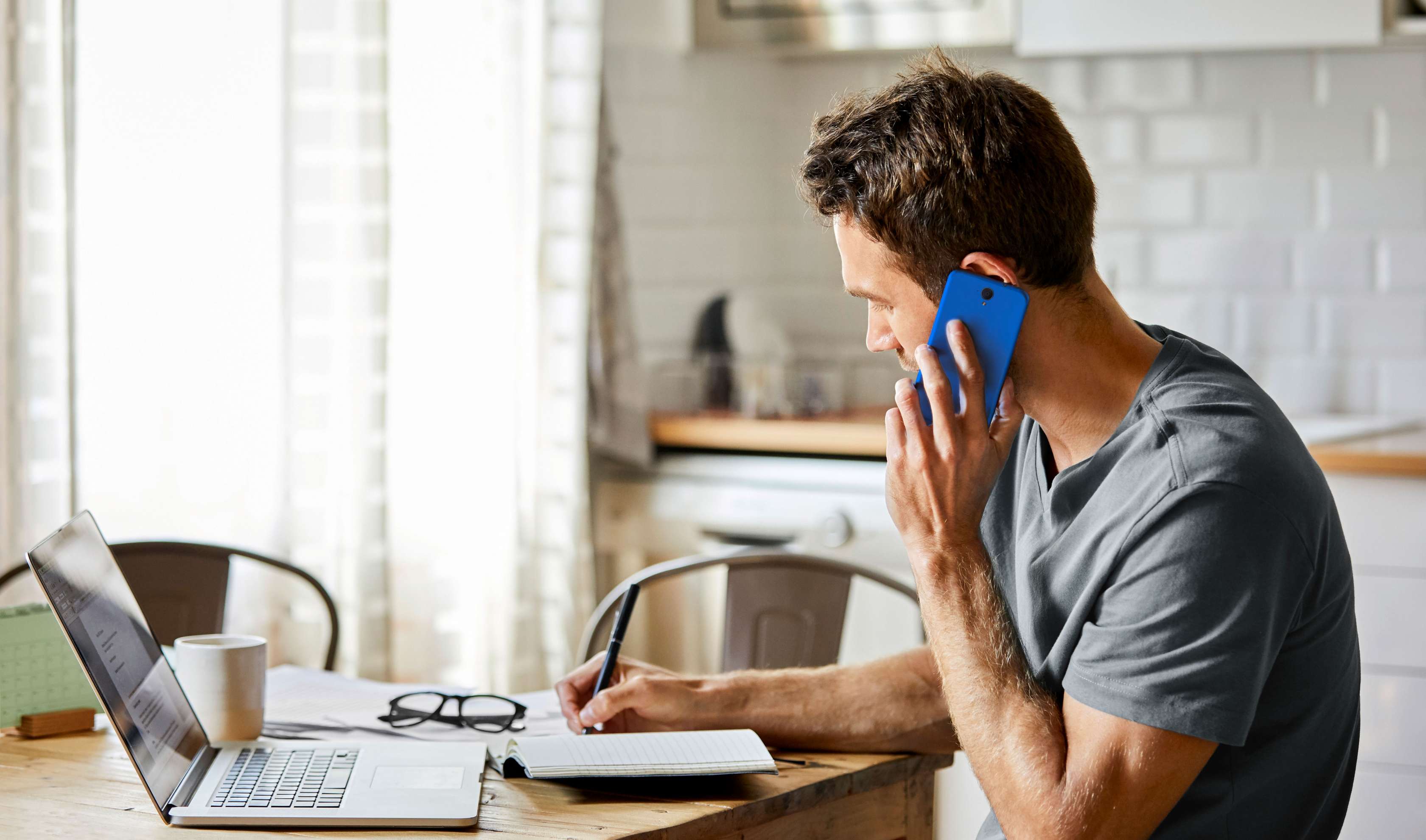 Allianz Rechtsschutzversicherung: Mann sitzt telefonierend vor seinem Laptop am Küchentisch.