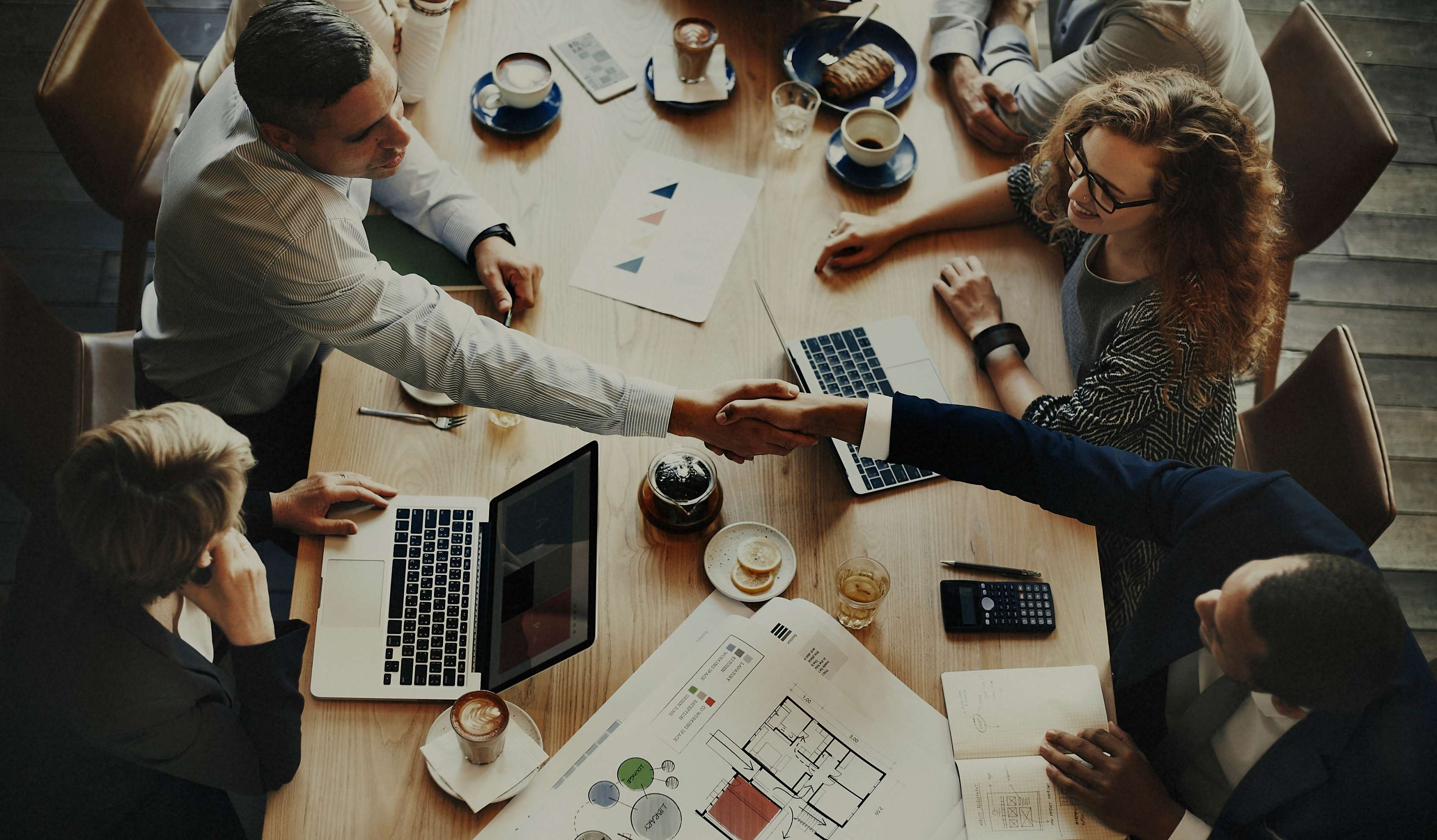 Allianz Rechtsschutzversicherung Arbeitsrecht: Gruppe von Personen sitzt an einem Tisch mit Laptops, zwei Männer reichen sich die Hand.