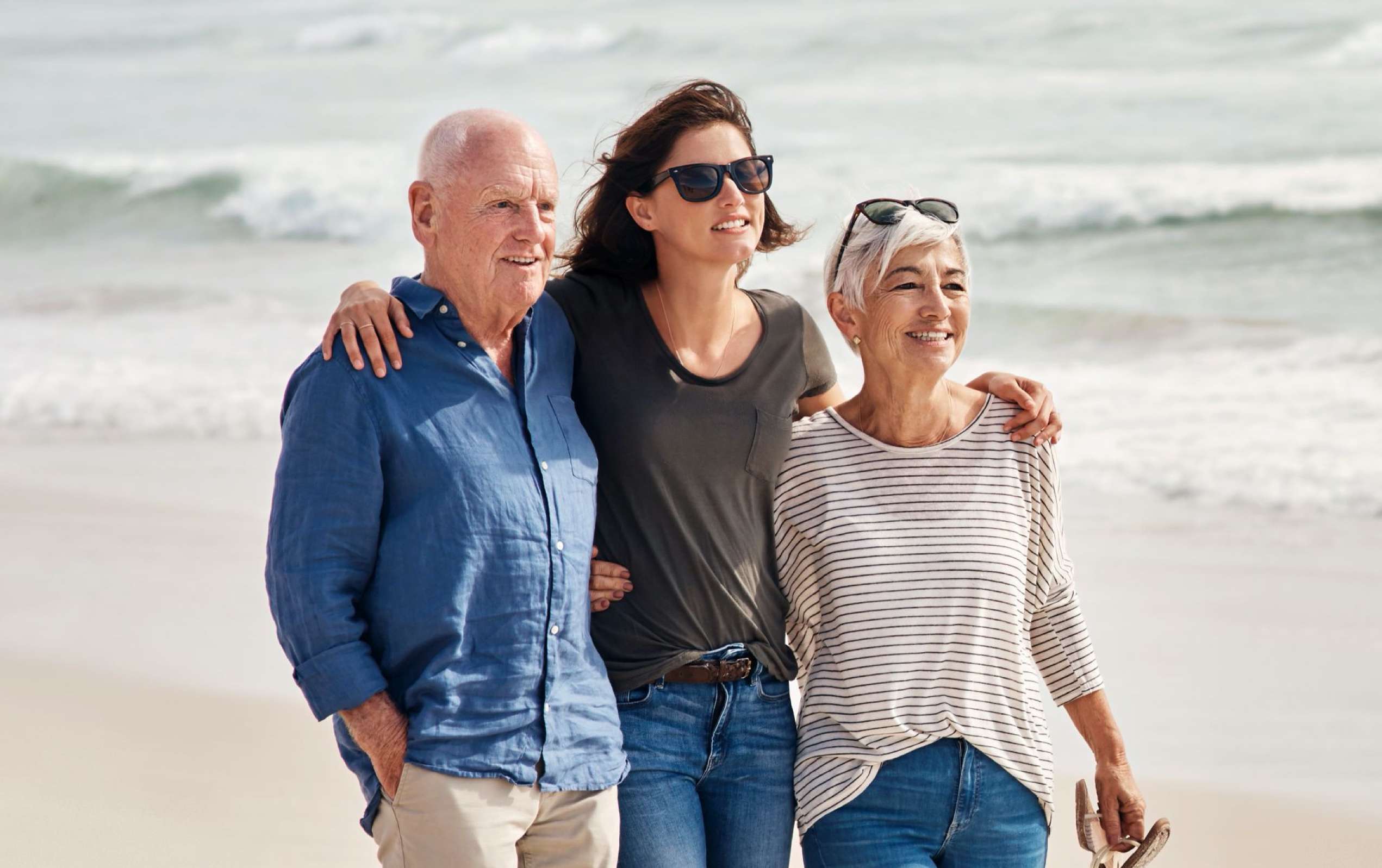 Alliant Patientenverfügung: Junge Frau geht Arm in Arm mit ihren Eltern am Strand entlang.