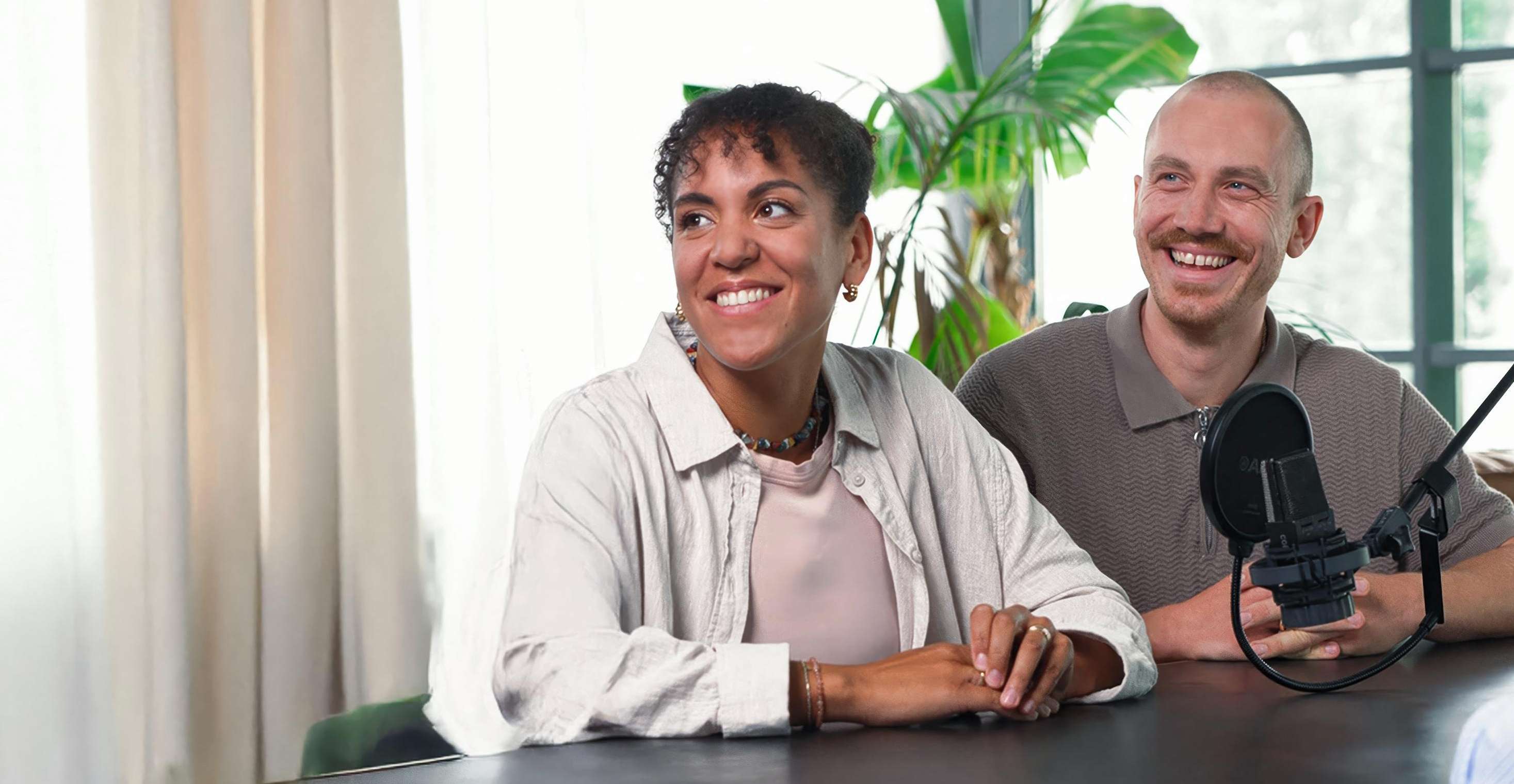 Eine Frau und ein Mann sitzen nebeneinander am Tisch, vor ihnen steht ein Mikrofon.