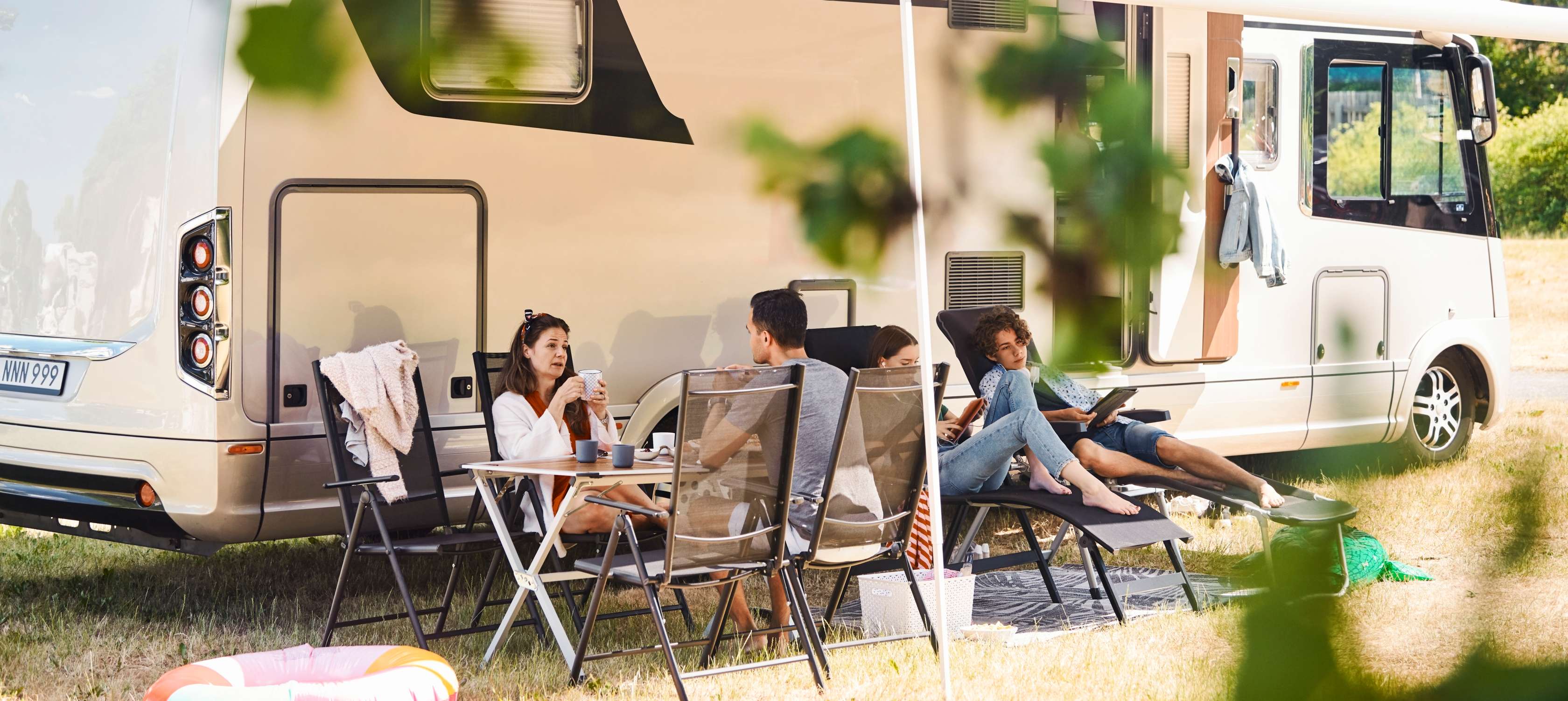 Allianz Dauercamping-Versicherung: Familie sitzt entspannt unter Vordach eines Wohnmobils