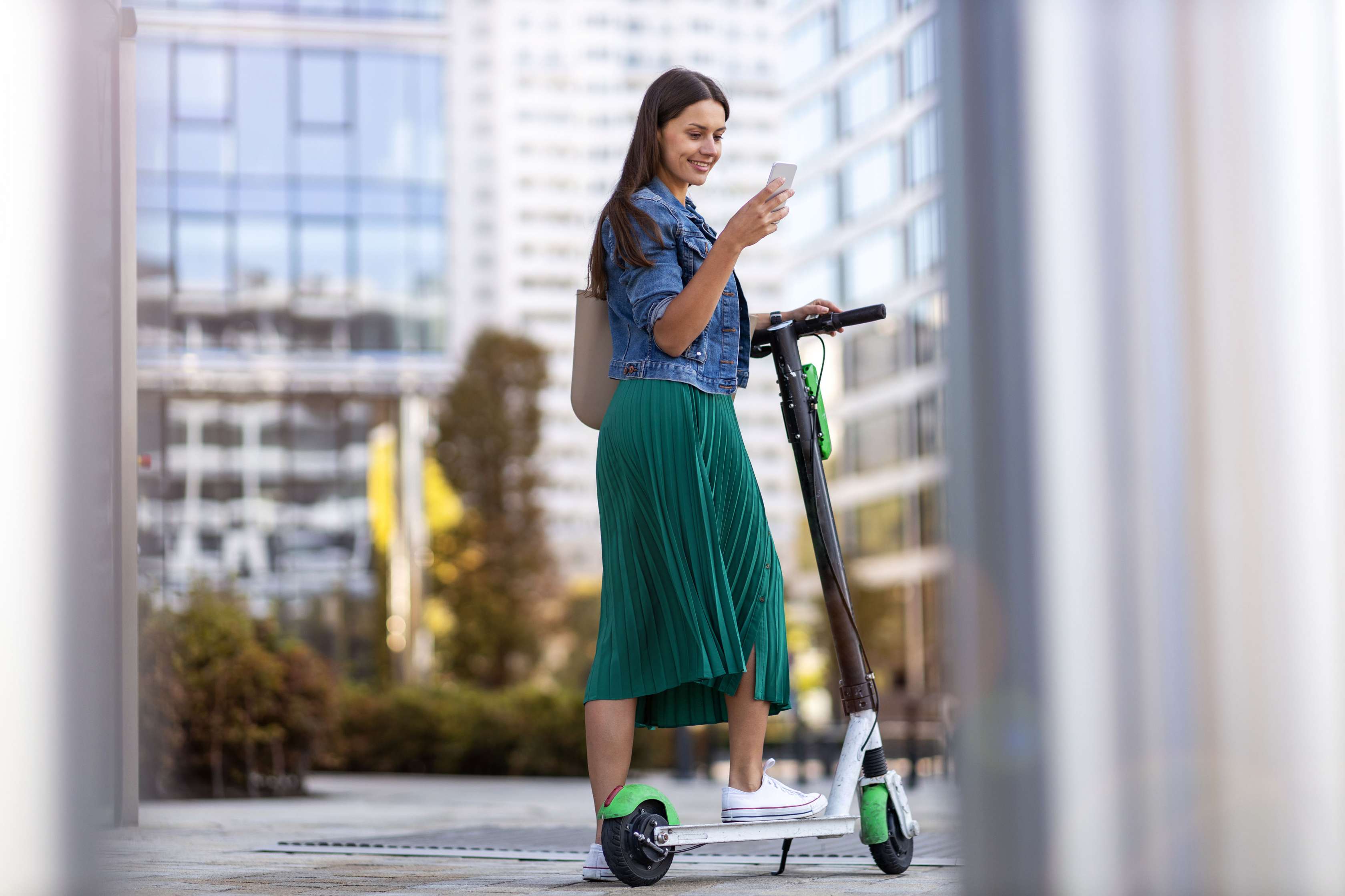 E-Scooter-Unfall: Frau steht auf abgestelltem E-Scooter und schaut auf ihr Mobiltelefon