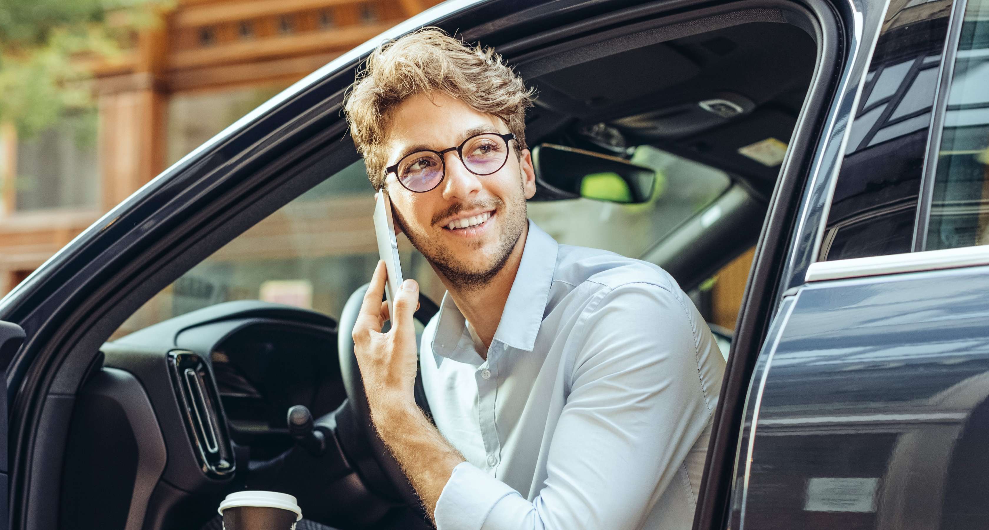 Auto verkauft Versicherung:  Ein Mann sitzt telefonierend in seinem Auto mit offener Tür