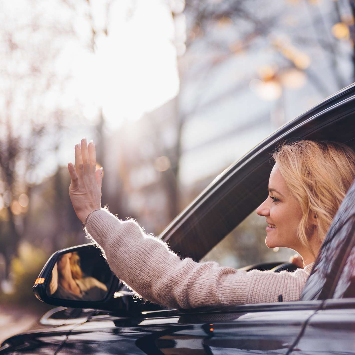 Allianz - Autoverleih: Blick auf das geöffnete Fenster eines Pkw, aus dem eine junge blonde Frau winkt