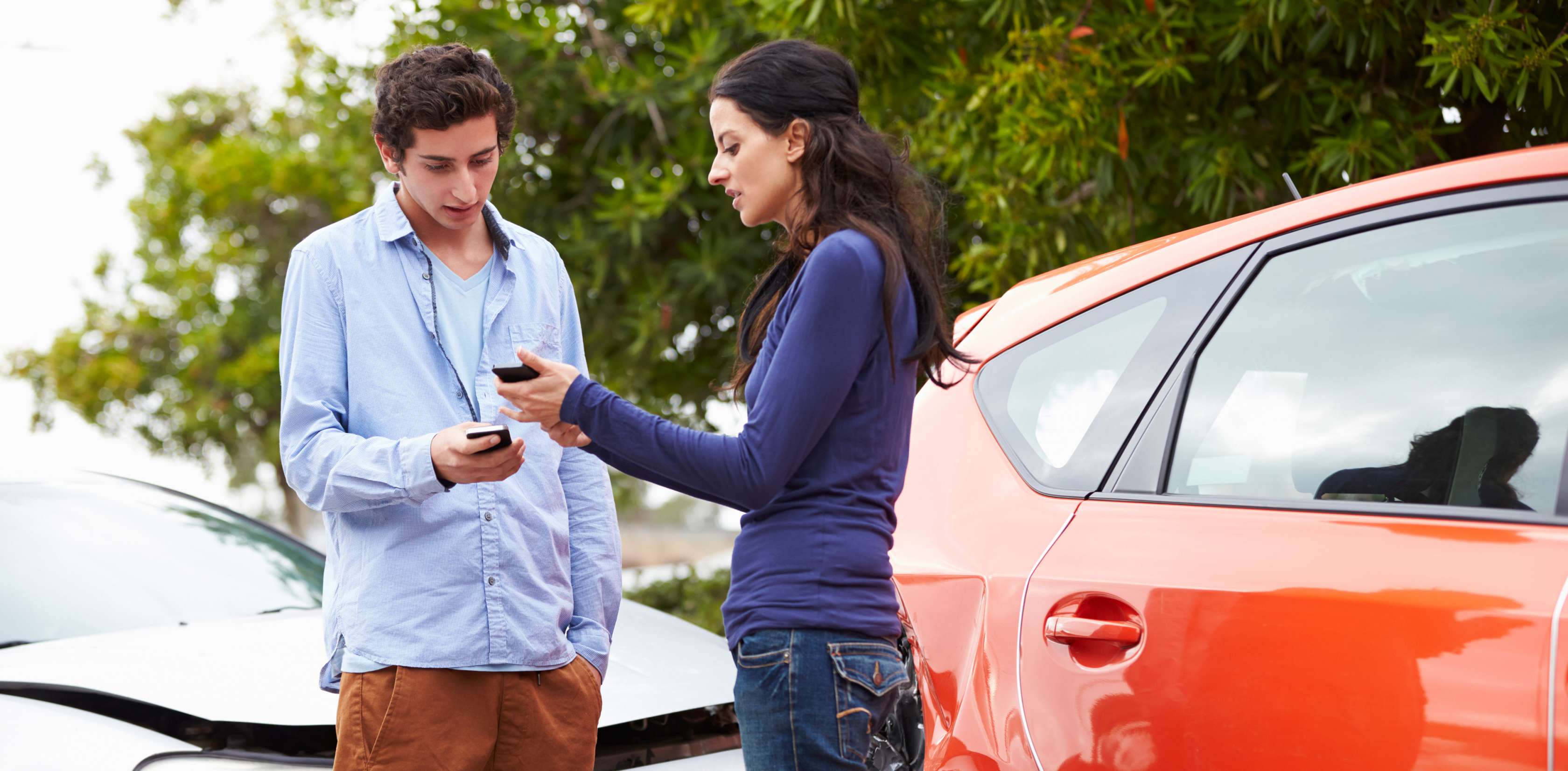 Mann und Frau mit Smartphones in der Hand stehen an Unfallstelle vor ihren Autos