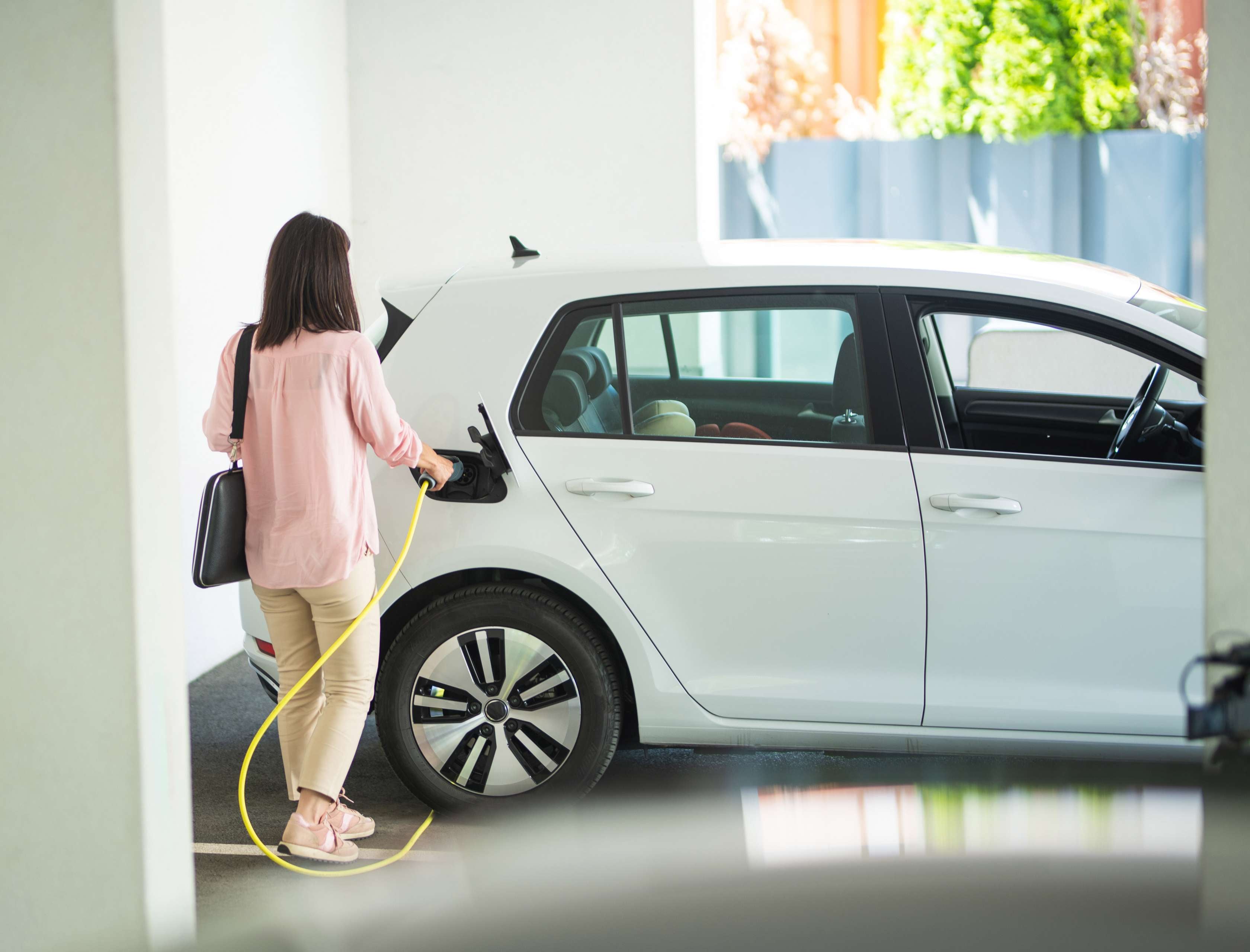 E-Auto Versicherung: Eine Frau steckt ein Ladekabel an ein Elektroauto in einer Garage.