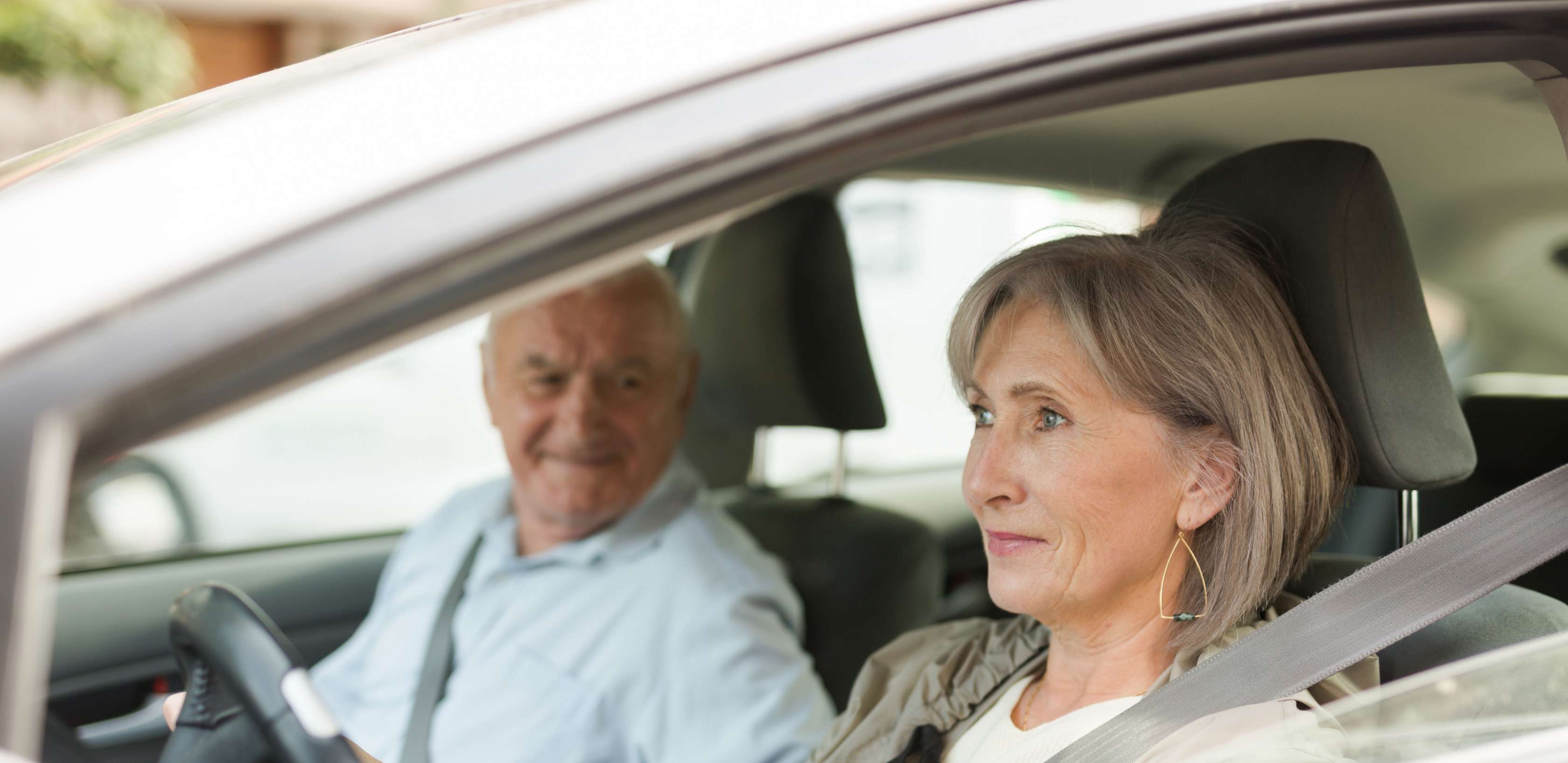 E-Autos für Senioren: Frau mit grauen Haaren steuert Pkw mit älterem Mann auf Beifahrersitz