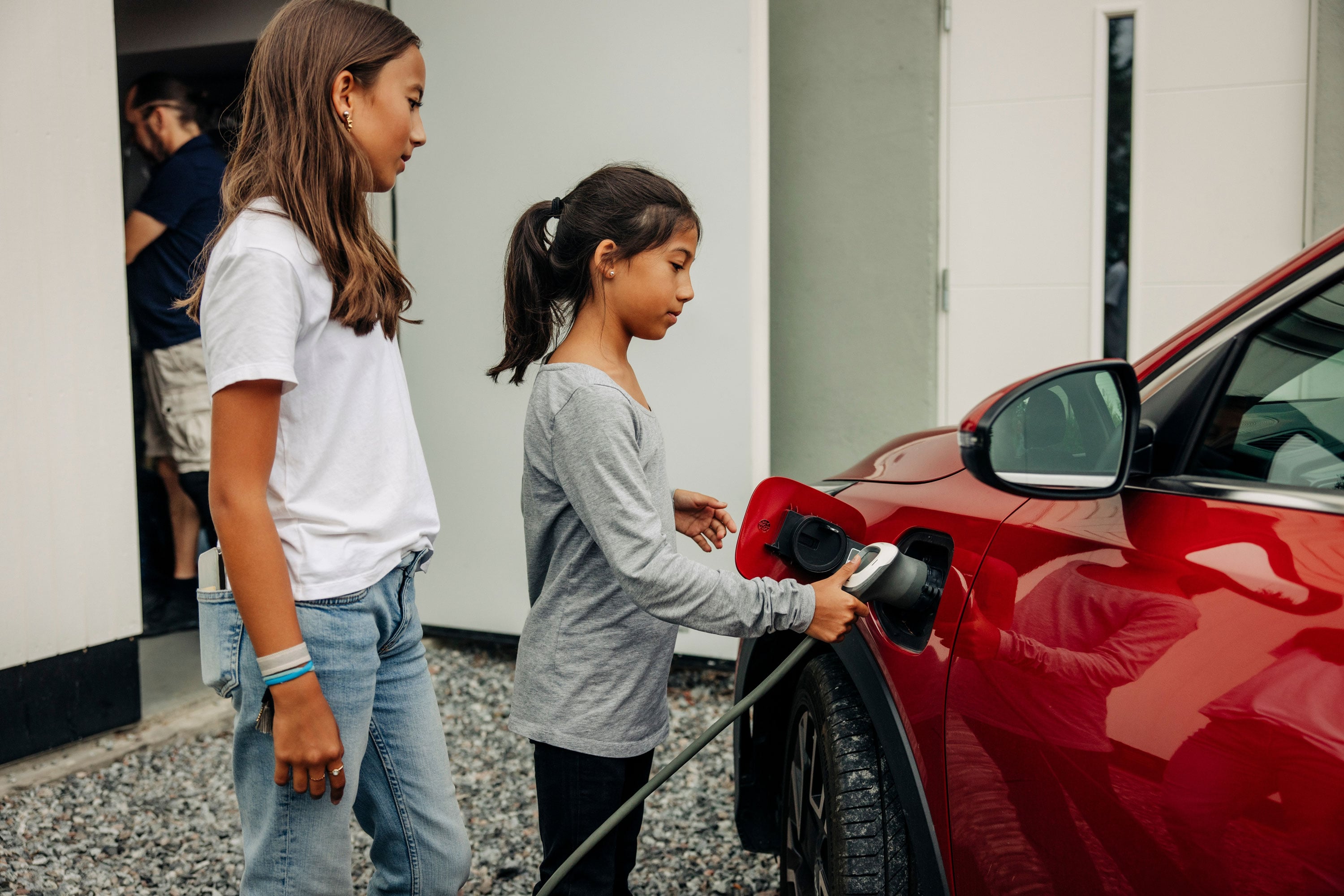 Elektroauto Vergleich: Zwei Kinder laden zusammen ein Elektroauto vor der Garage.