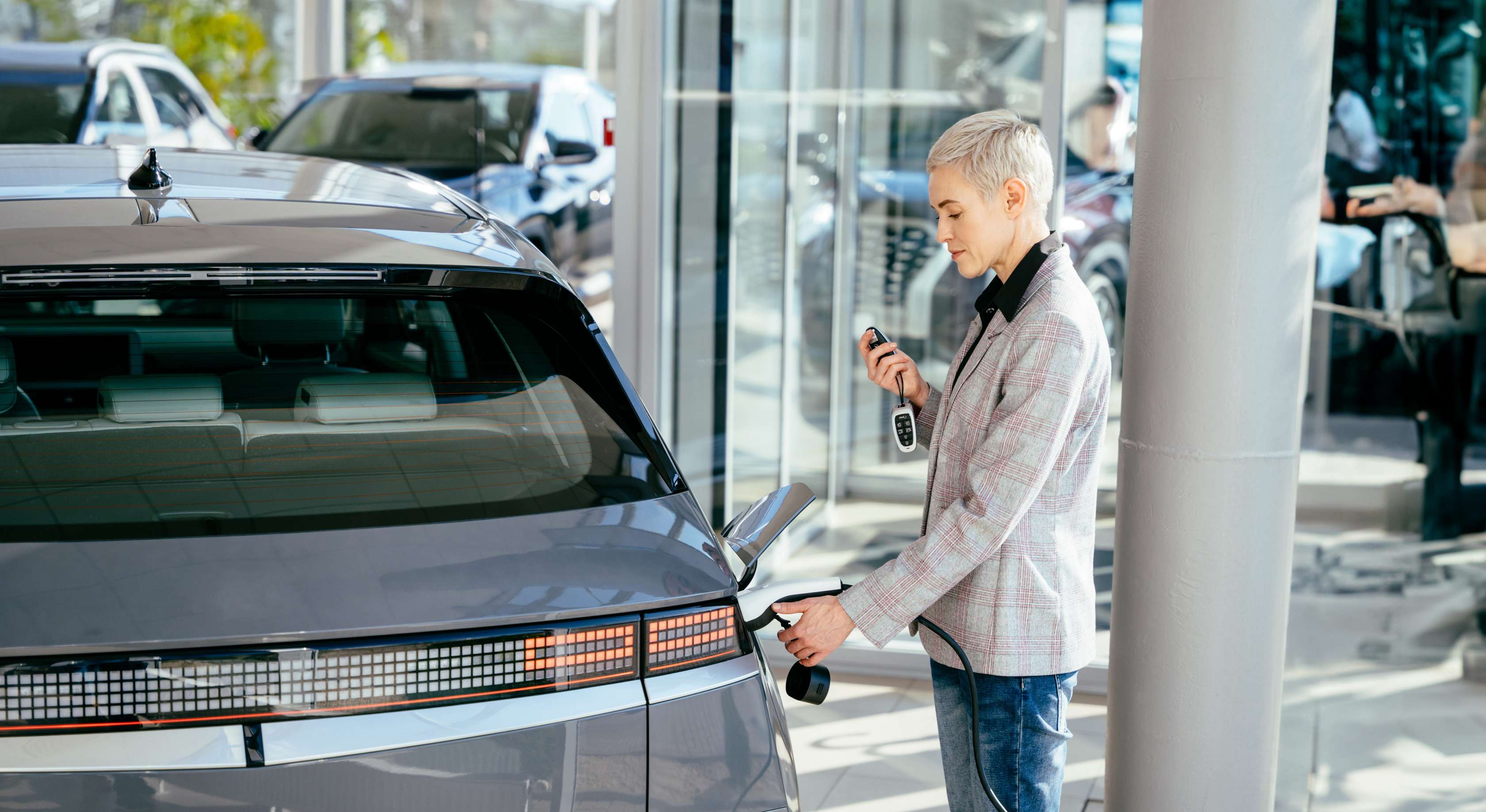 Wertverlust Elektroauto: Frau verbindet Ladekabel mit E-Auto und hält Autoschlüssel in der Hand