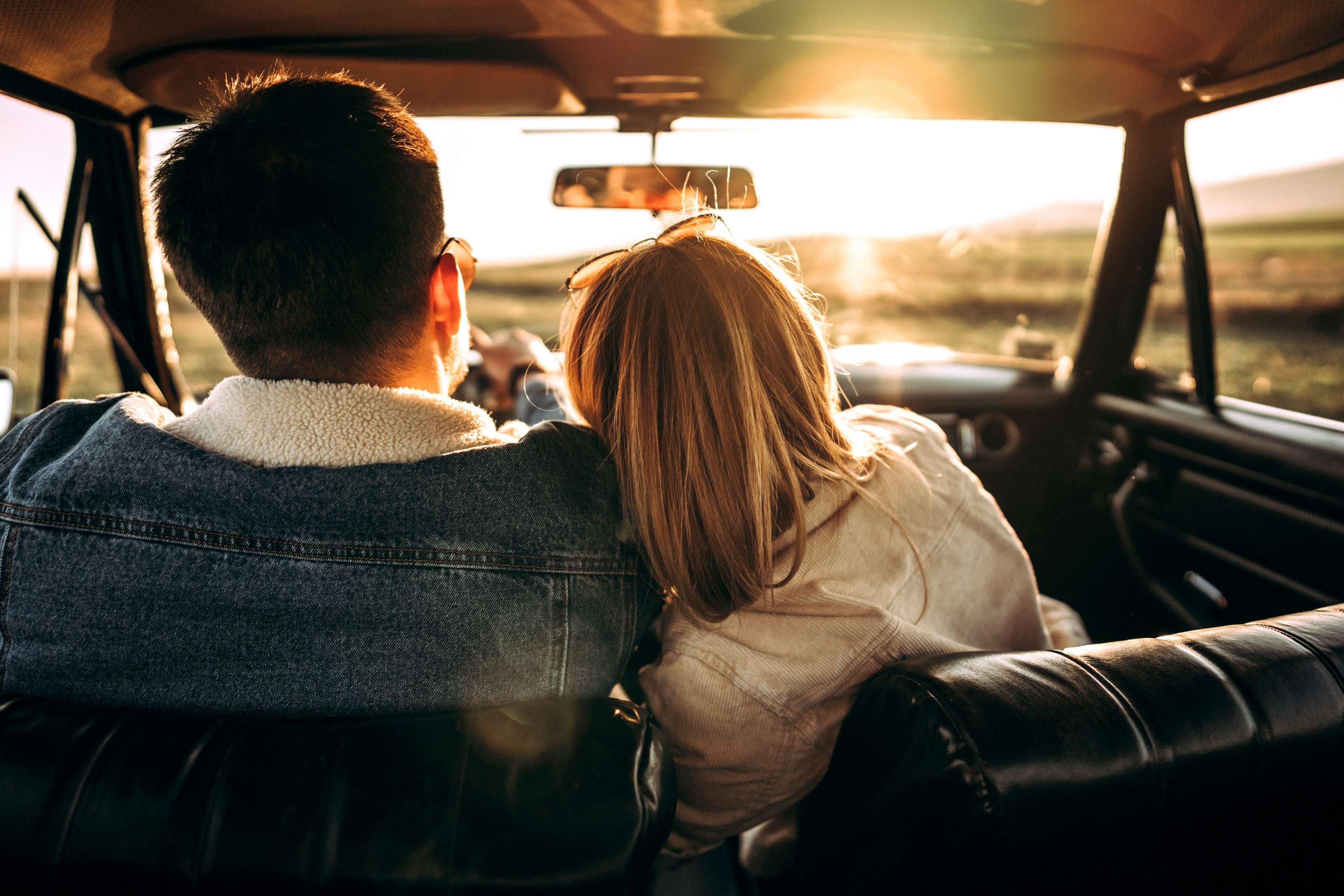 Fahrerschutz Versicherung: Frau auf Beifahrersitz lehnt sich an Mann, der am Steuer des Pkw sitzt