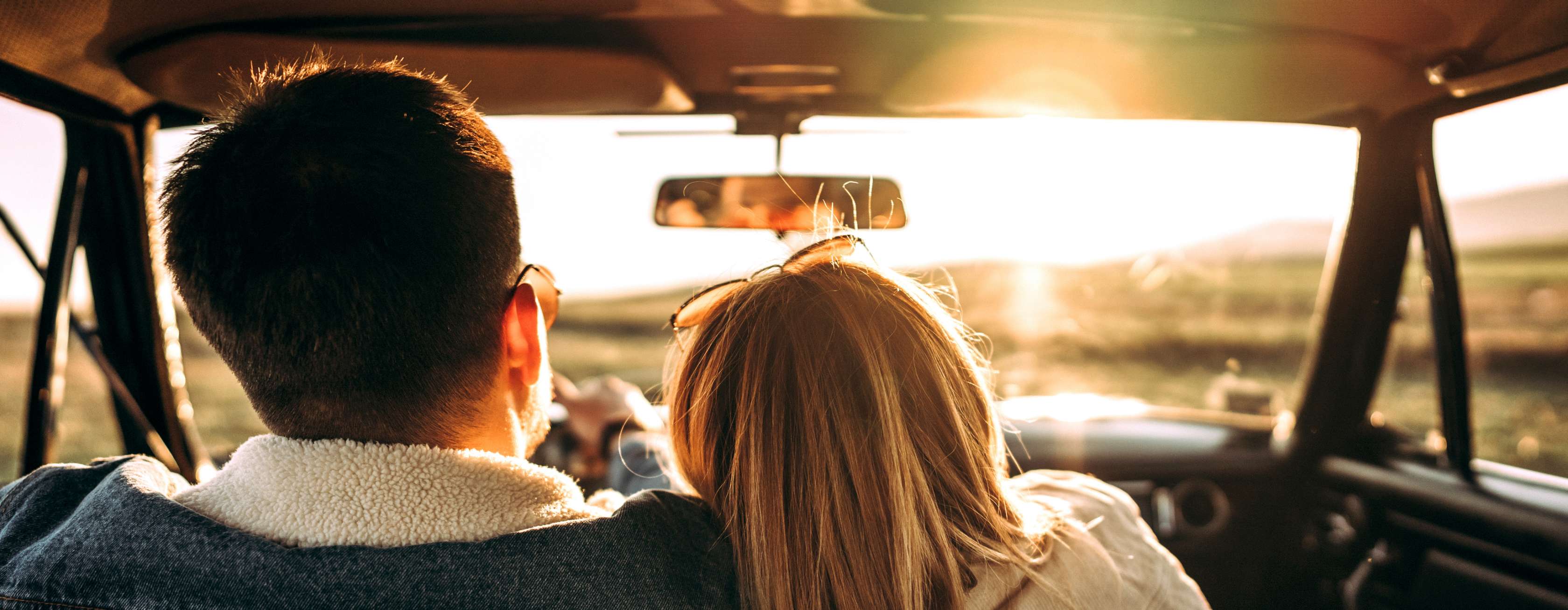 Fahrerschutz Versicherung: Frau auf Beifahrersitz lehnt sich an Mann, der am Steuer des Pkw sitzt