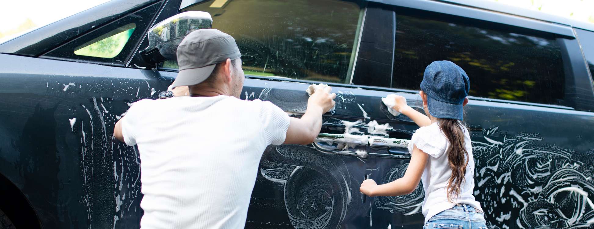 Mann putzt mit seiner Tochter ein dunkelblaues Auto