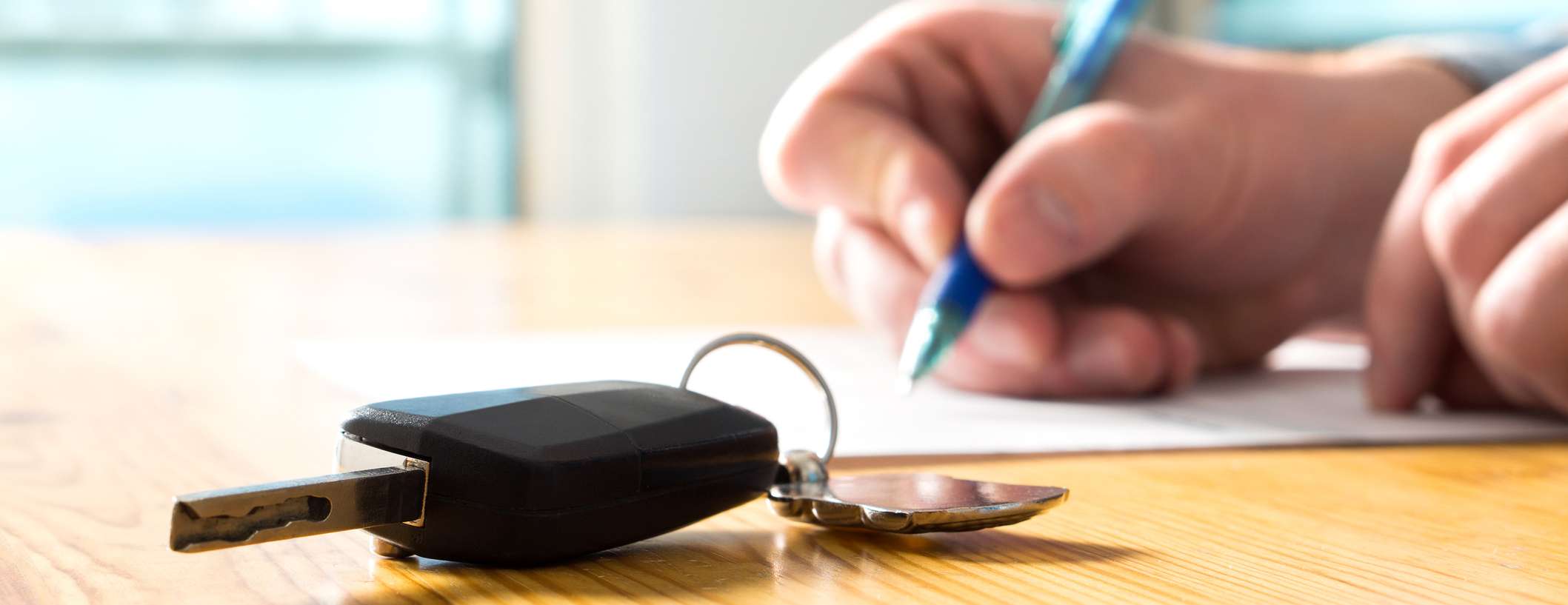 Autoschlüssel liegt auf Holztisch, während Person Vertrag unterschreibt