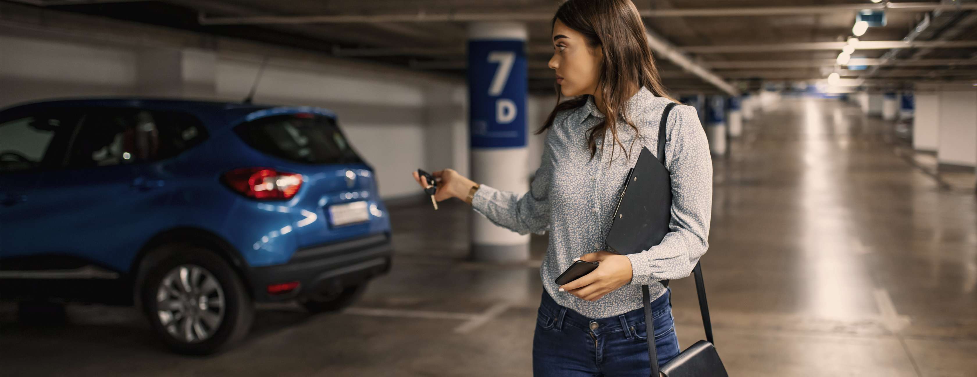 Junge Frau verriegelt mit Funkschlüssel blauen SUV in öffentlicher Tiefgarage