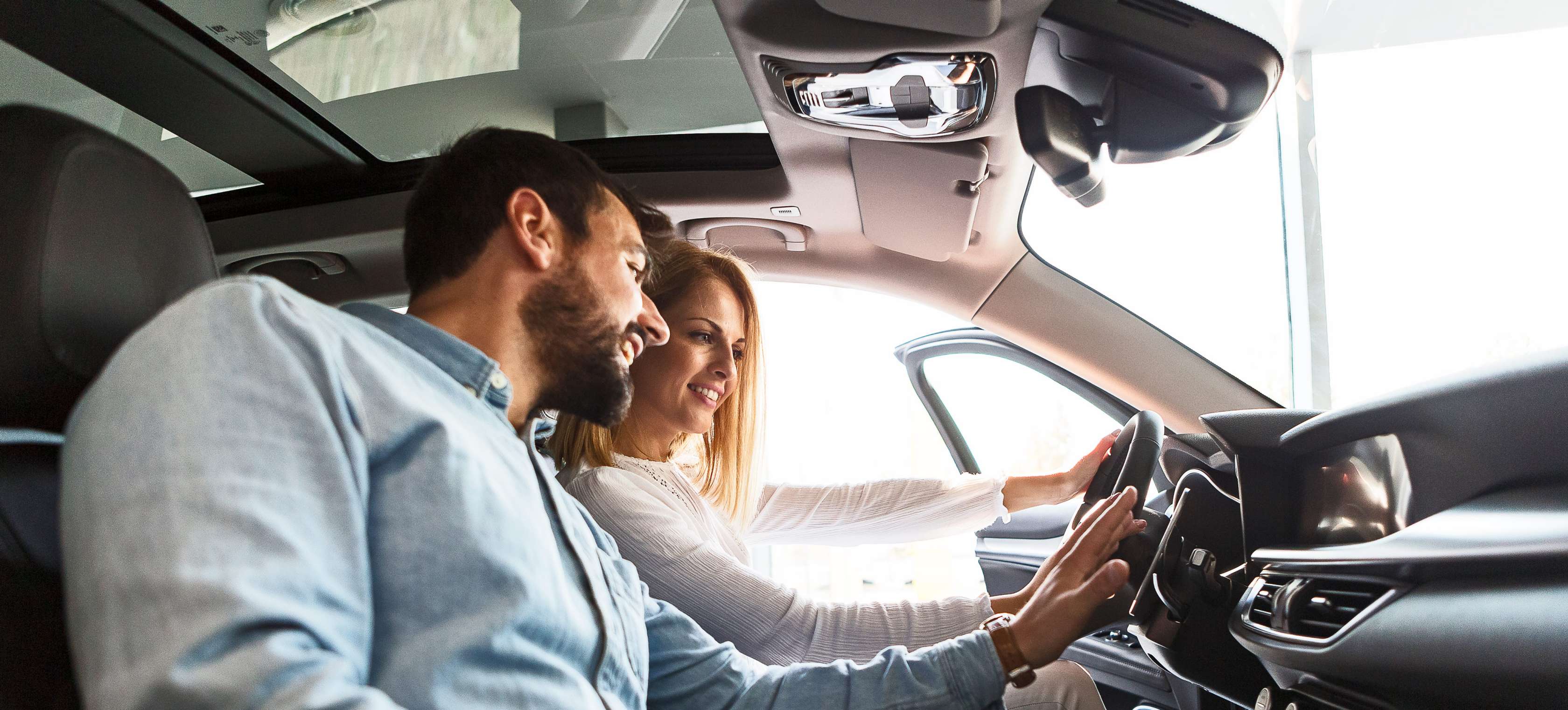 Fahrzeugwechsel-Versicherung: Frau und Mann sitzen in Auto und tippen auf Display im Armaturenbrett