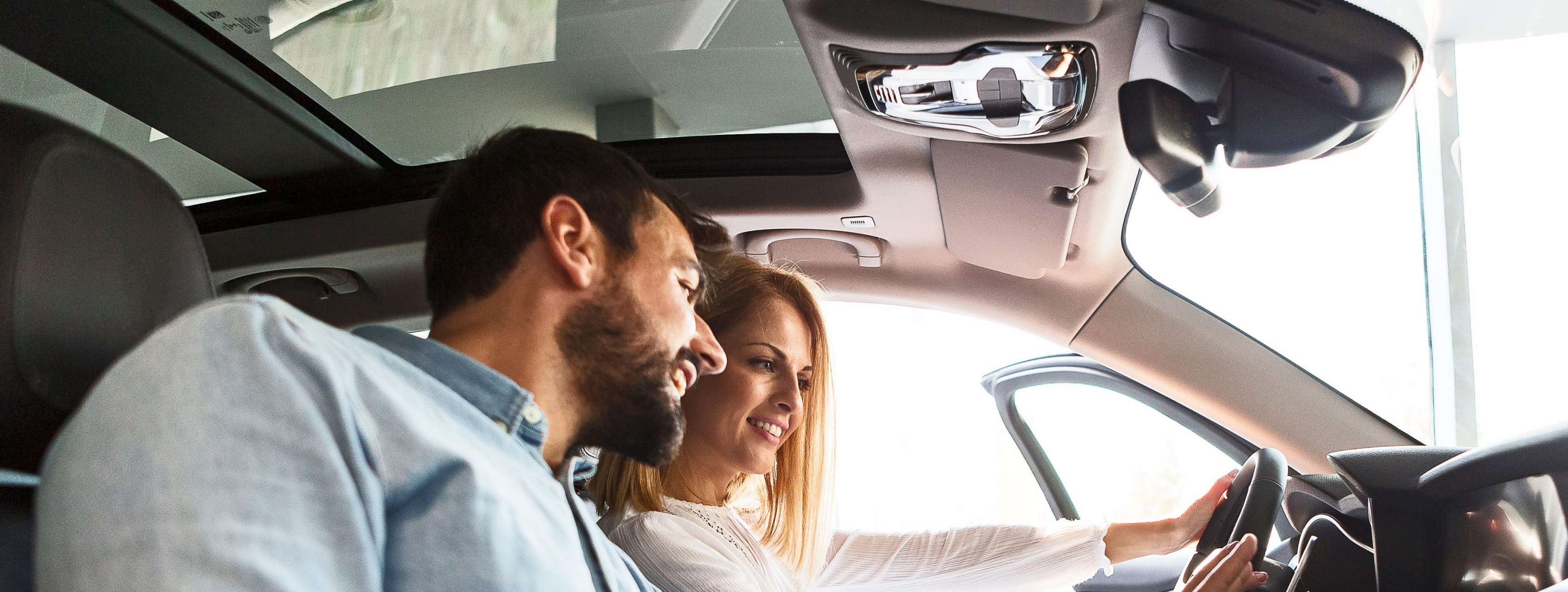 Fahrzeugwechsel-Versicherung: Frau und Mann sitzen in Auto und tippen auf Display im Armaturenbrett