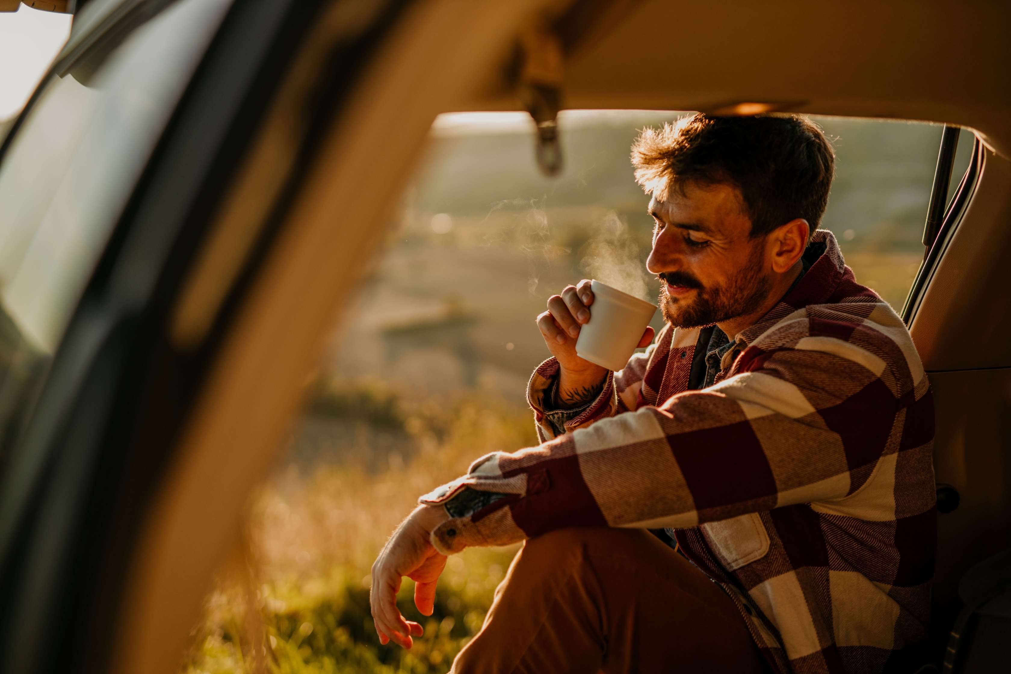 Kfz-Haftpflichtversicherung: Mann sitzt im Auto und trinkt Kaffee