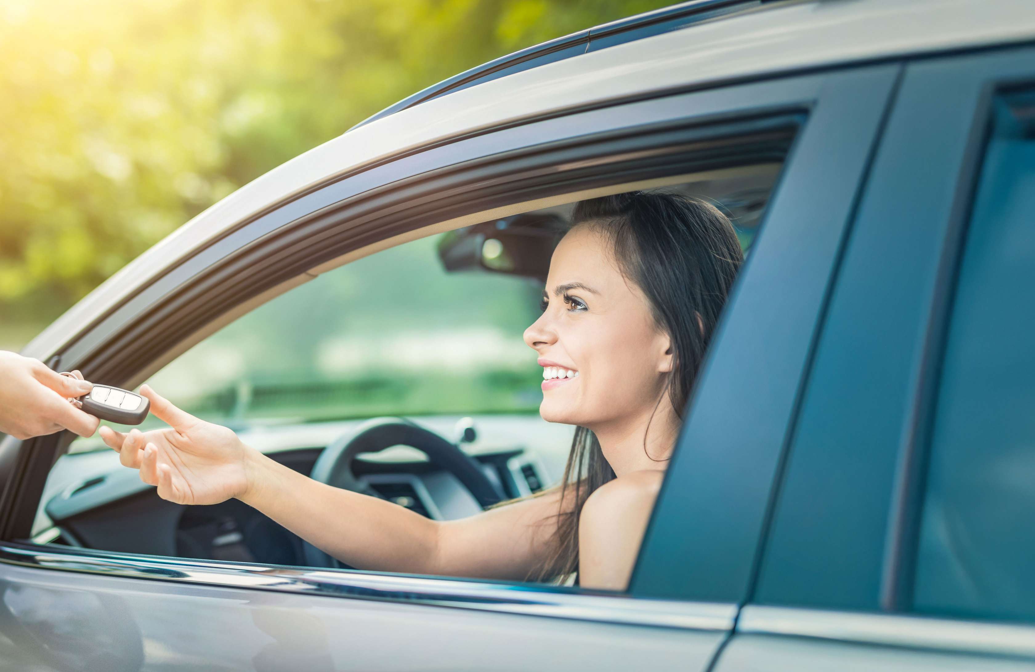 Bei Kfz-Halterwechsel übergibt jemand einer jungen Frau, die im Auto sitzt, durch das geöffnete Fahrerfenster den Autoschlüssel