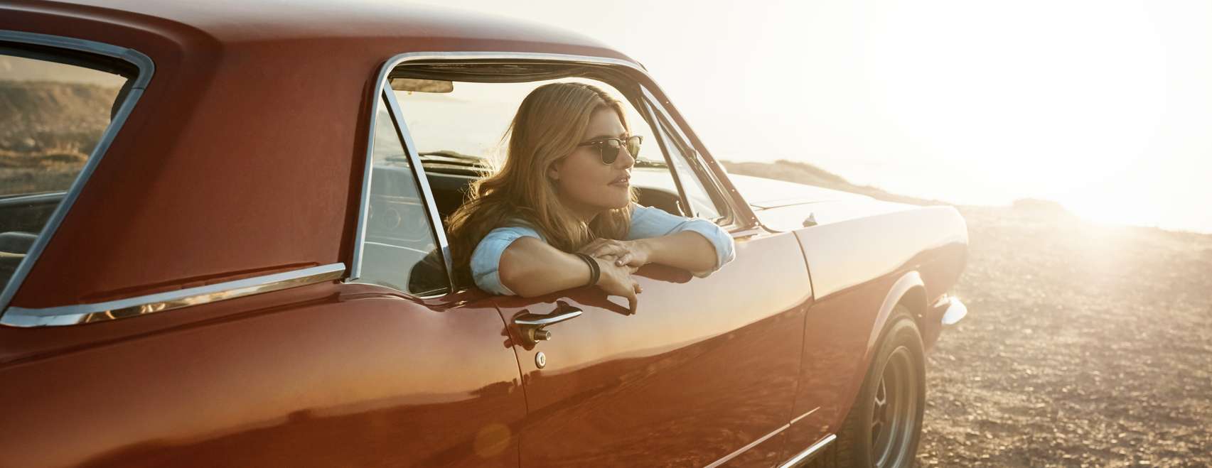 Frau mit Sonnenbrille blickt am Meer aus Autofenster