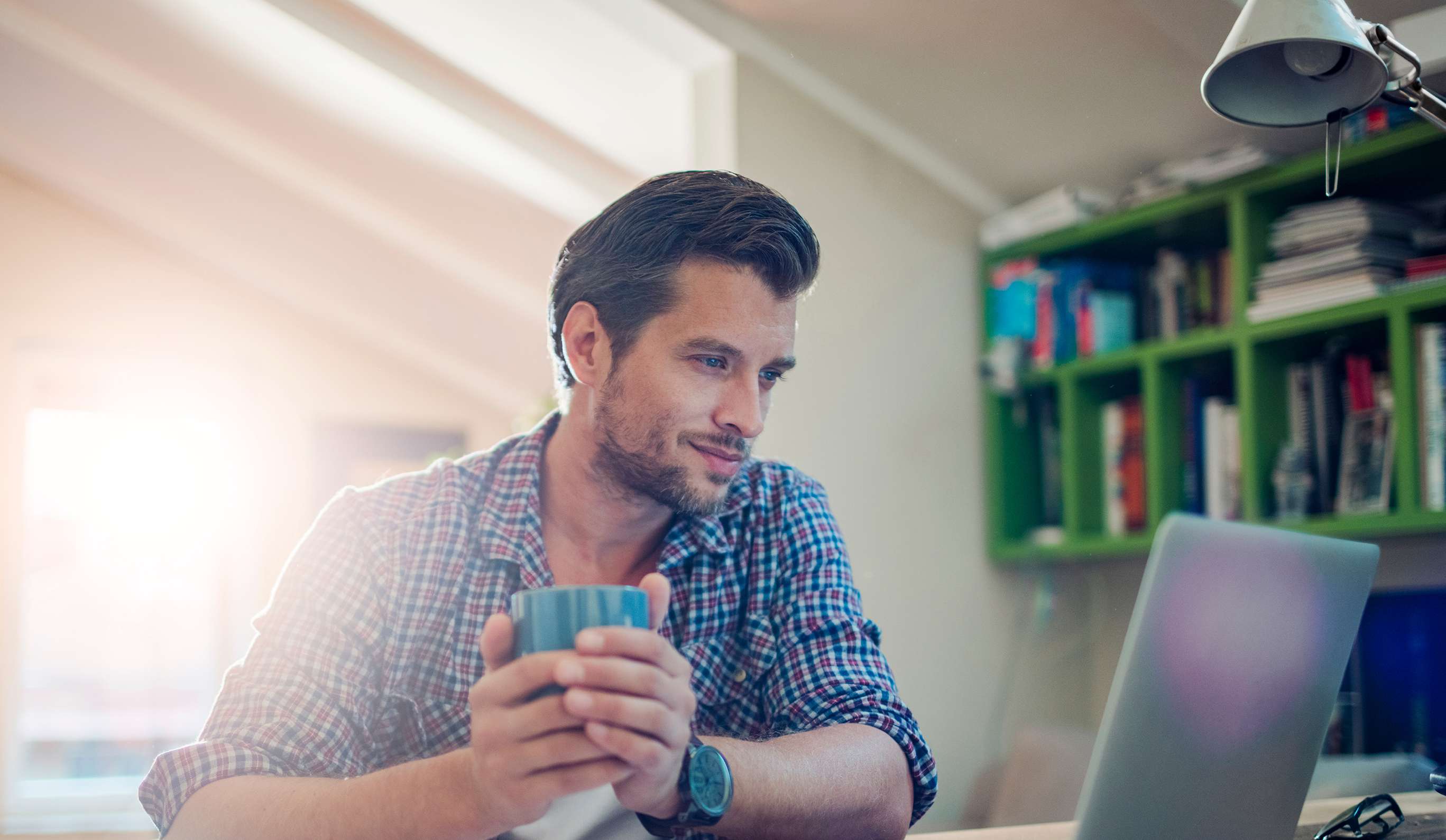 Kfz-Versicherung kündigen: Mann sitzt mit einer Tasse Kaffee vor aufgeschlagenem Laptop