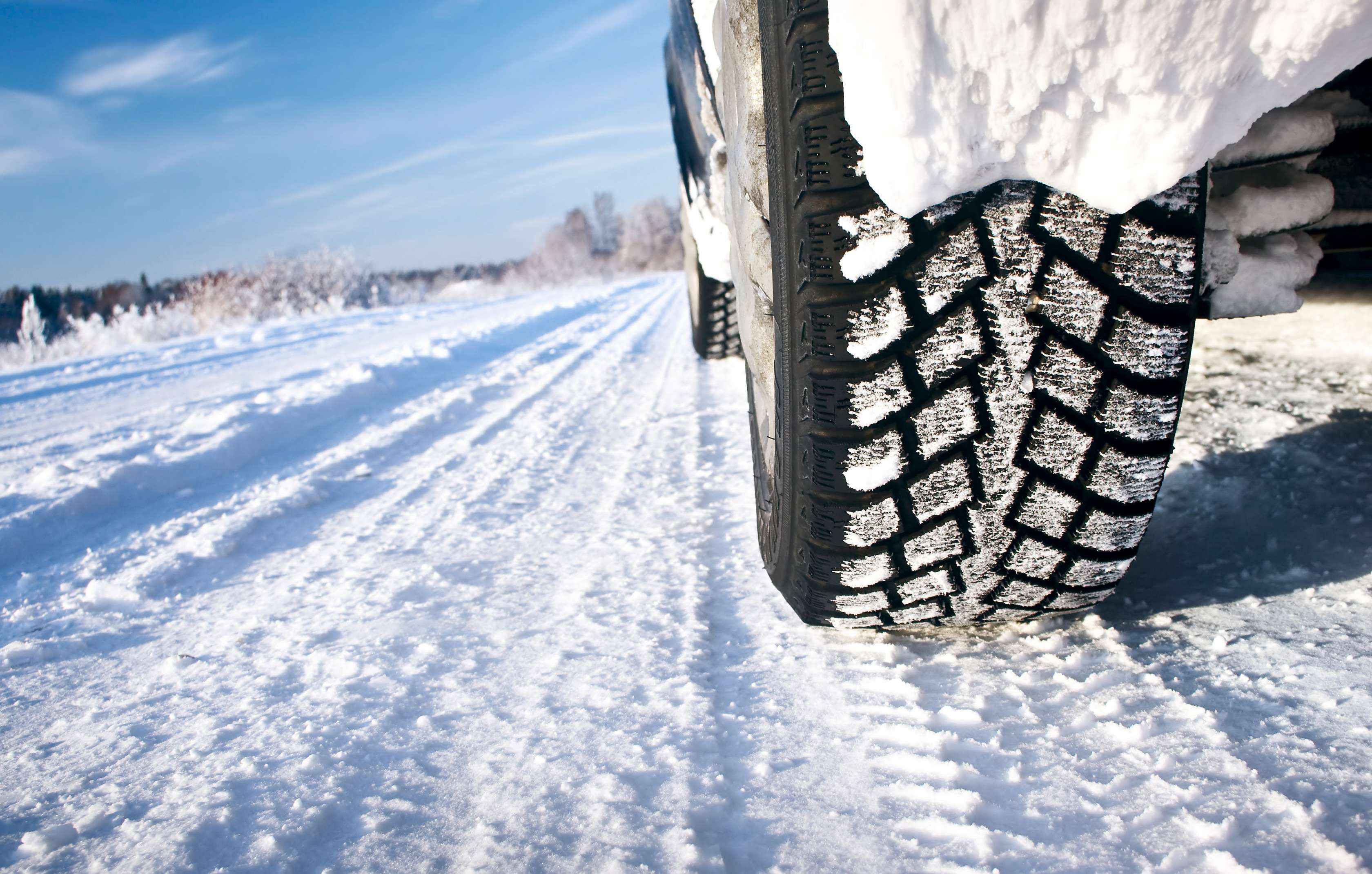 Allianz - Mindestprofiltiefe Winterreifen: Nahaufnahme des Hinterreifens eines Pkw, der im Winter auf schneebedeckter Straße fährt