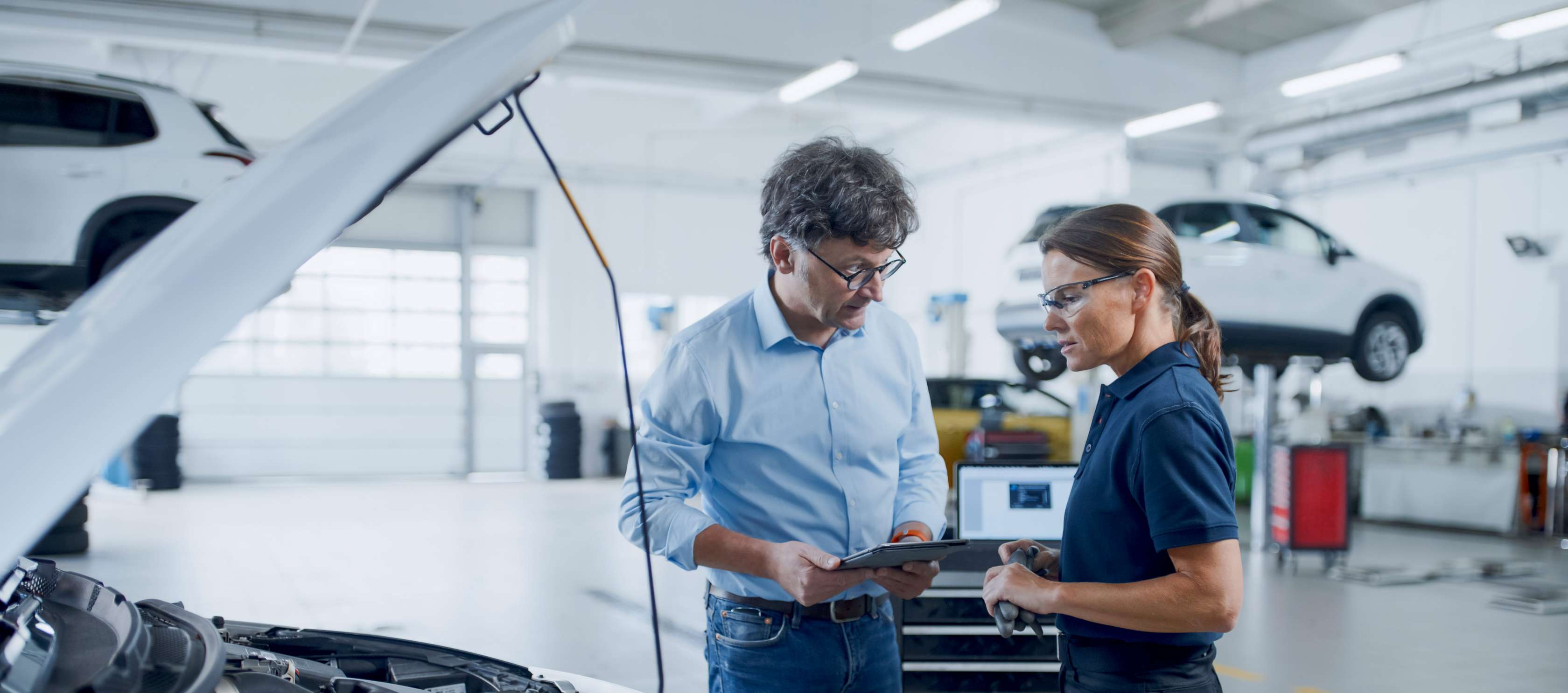 Nutzungsausfallentschädigung: Ein Mann steht mit einer Mechanikerin in einer KFZ-Werkstatt