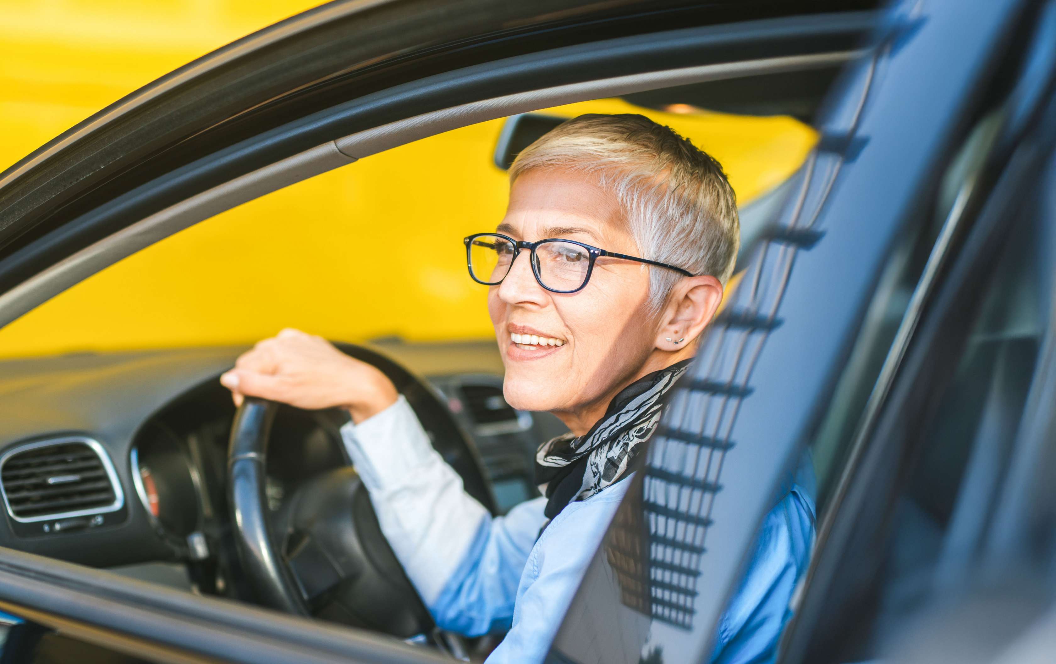 Kfz-Versicherung für Senioren: Ältere Frau sitzt lächelnd am Steuer eines Autos