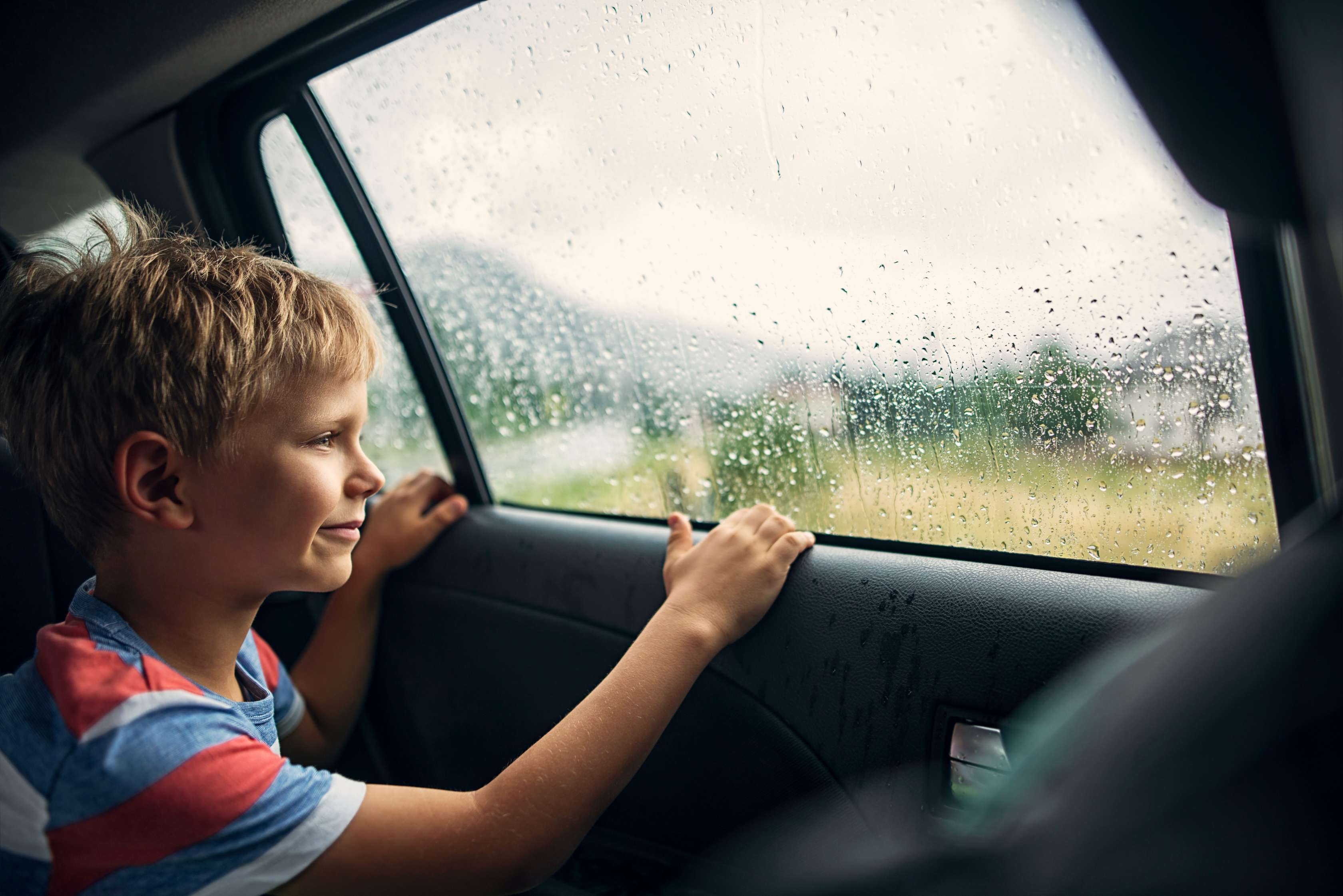 Teilkasko: Blonder Junge sitzt auf Rückbank eines Autos und blickt aus dem Fenster