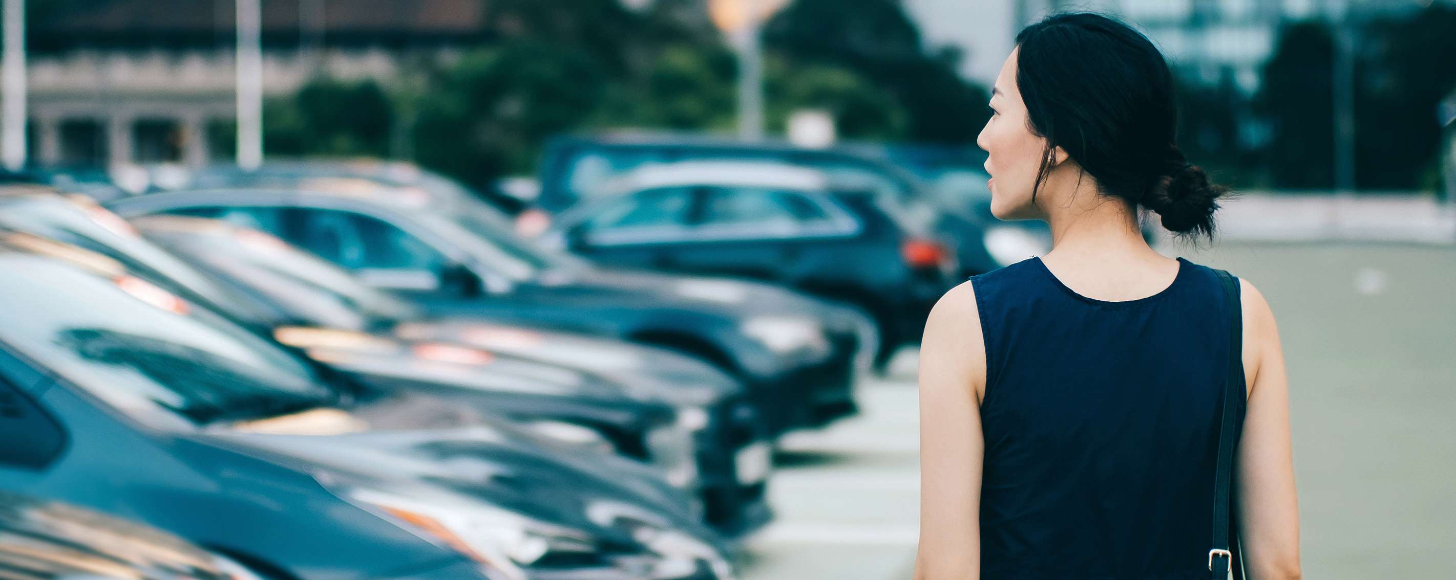 Frau läuft auf Parkplatz an Autos verschiedenster Typklassen vorbei