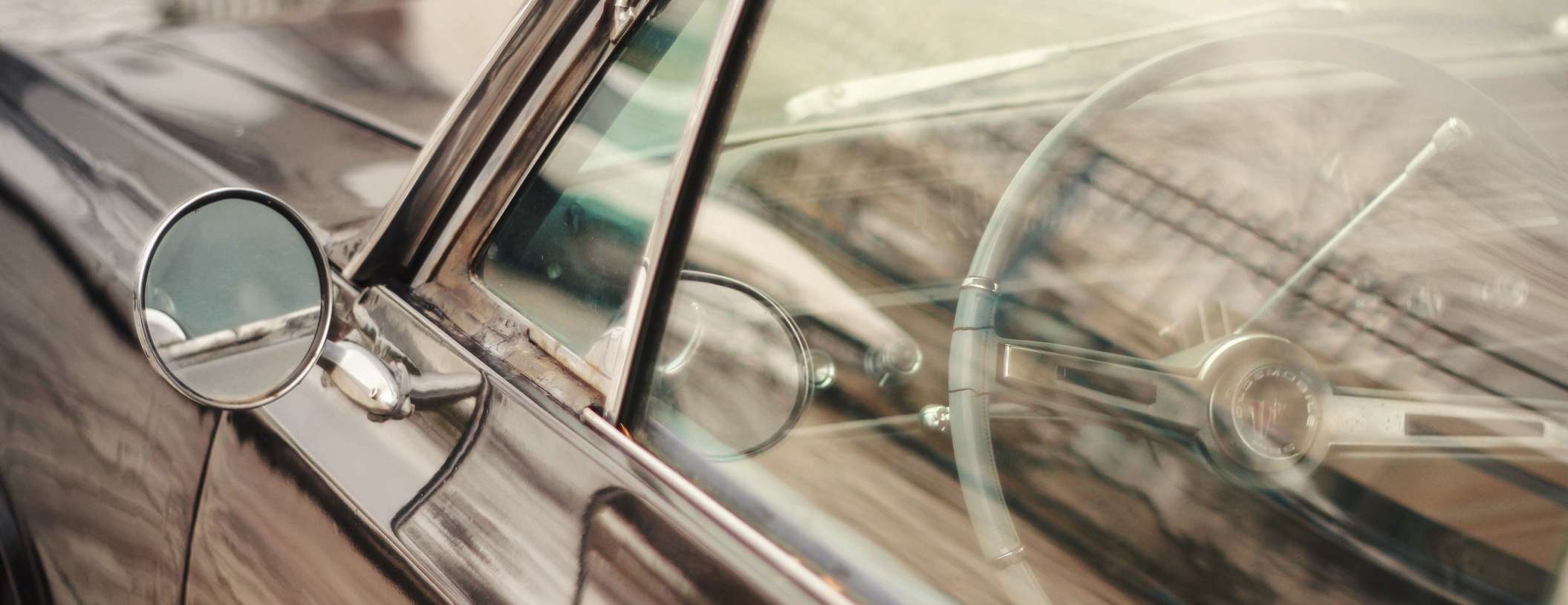 Blick auf Seitenspiegel, Fahrerfenster und Lenkrad eines schwarzen Oldtimers