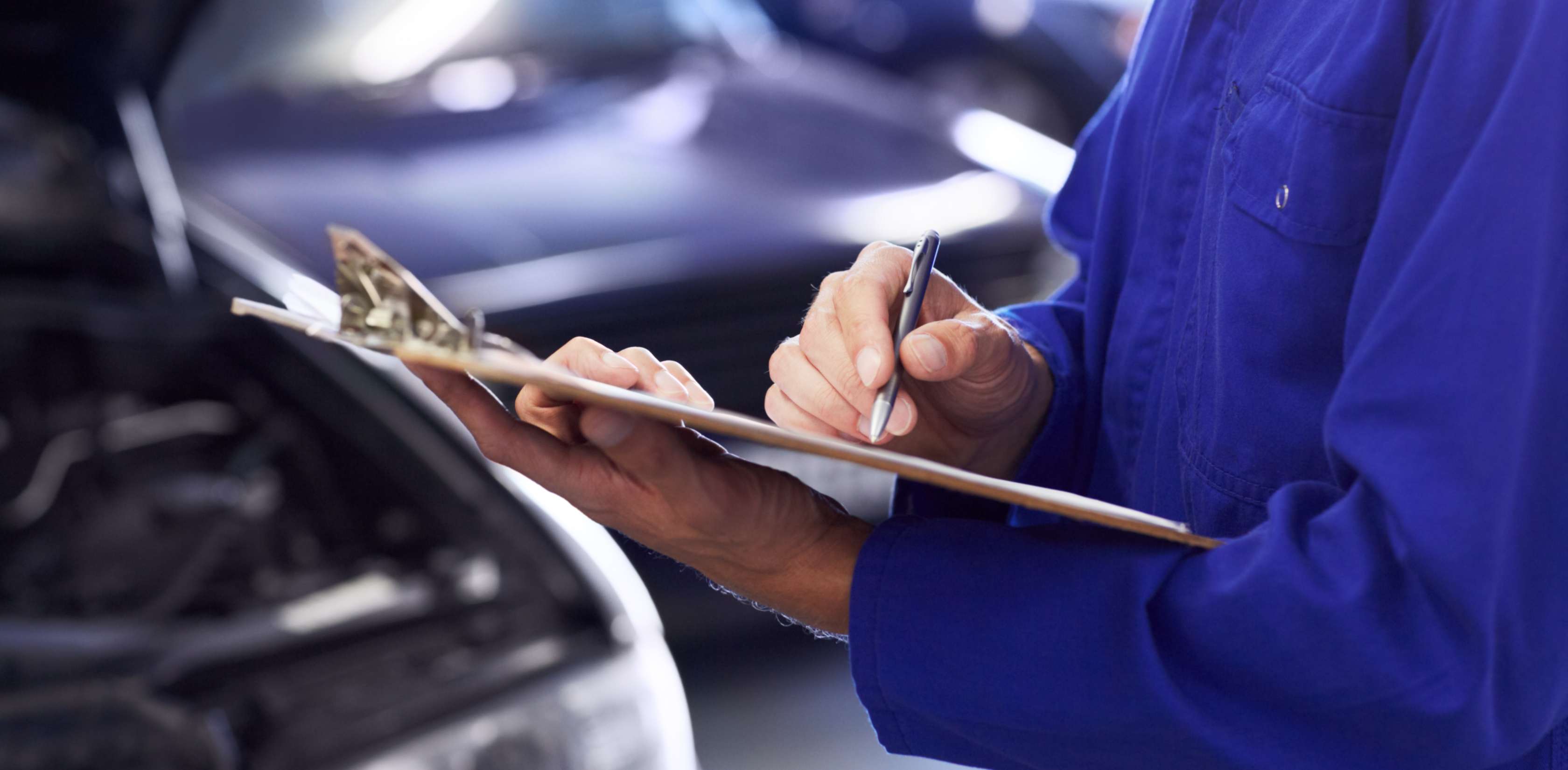 Gutachter in blauer Arbeitsmontur notiert Schäden an Auto, um Wiederbeschaffungswert zu berechnen